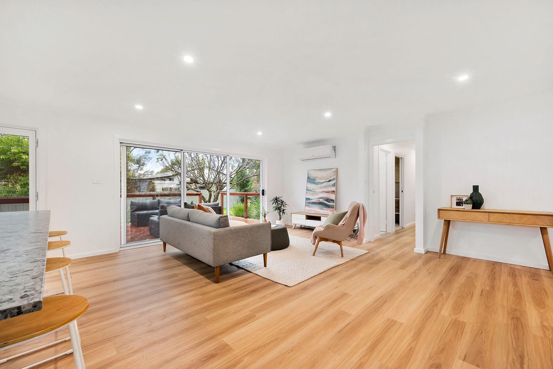 Open-plan living space with wood flooring, gray sofa, sliding doors to patio, and neutral decor.