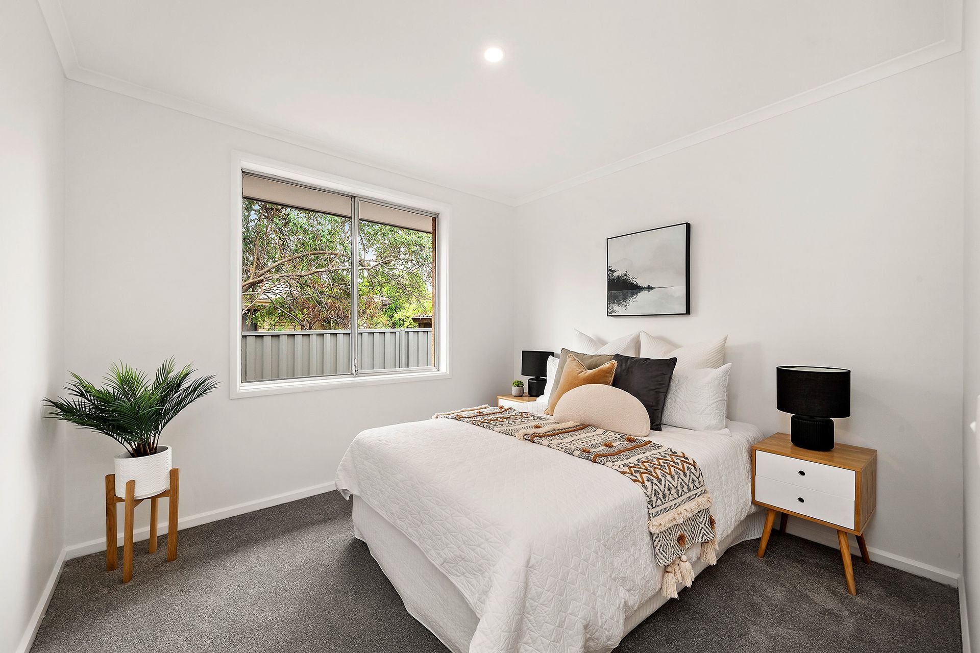 Backyard with lawn, brick house, white bench, fire pit, and green fences under a sunny sky.