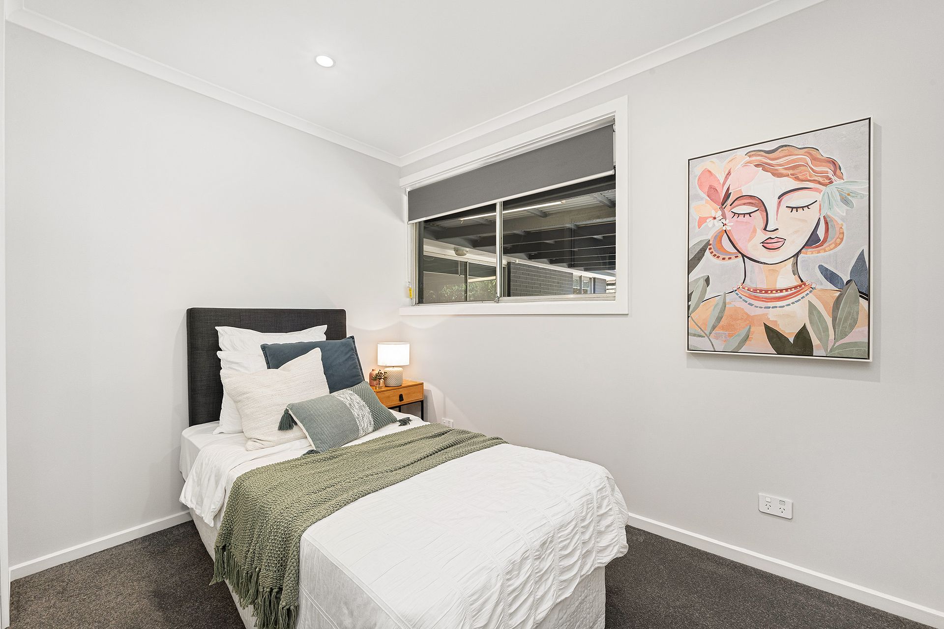 Bedroom with a single bed, artwork, and window. Gray walls and carpet.