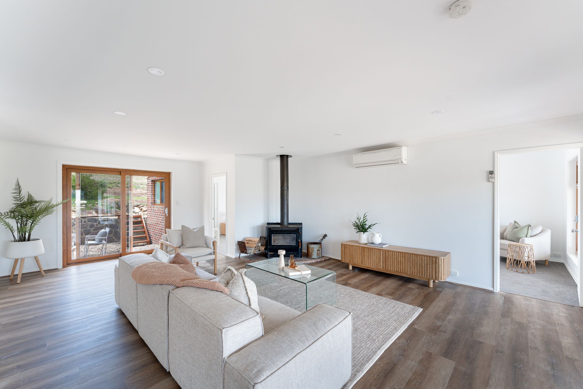 Spacious living room with white walls, fireplace, wood floors, and a light-colored sofa.
