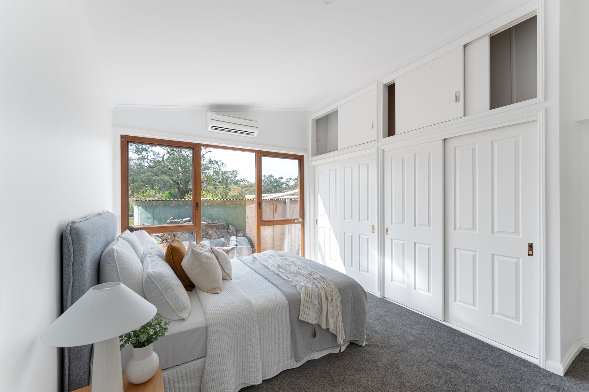 Bedroom with bed, large window, built-in white closet, and gray carpet.