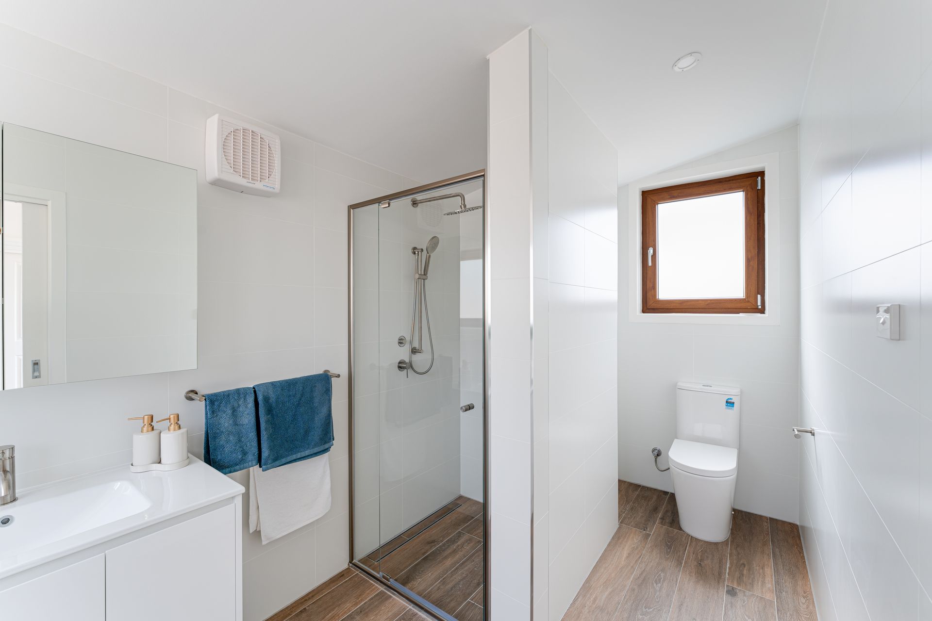 Bright white bathroom with glass shower, toilet, and window with wood trim.
