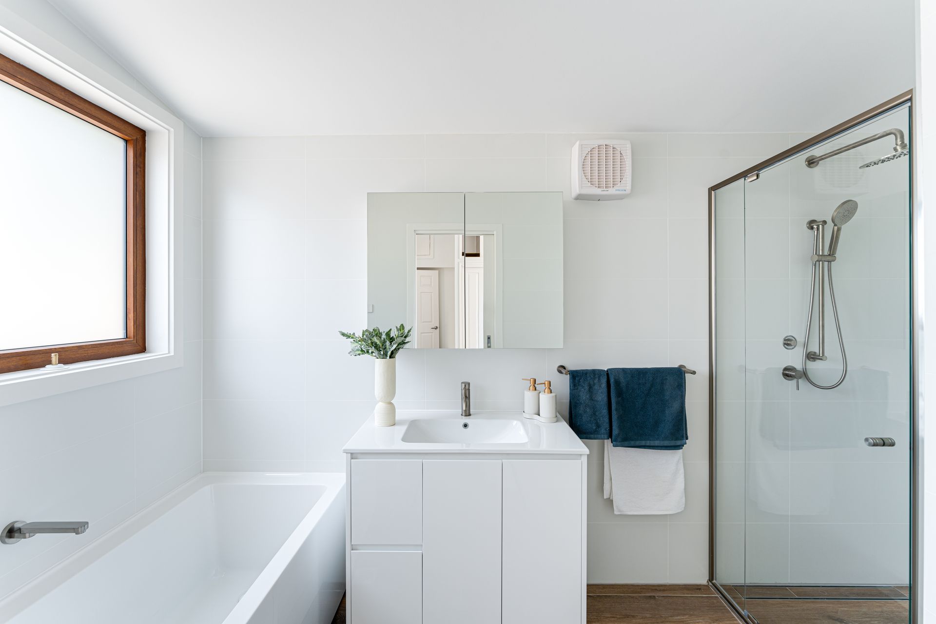 White bathroom with tub, vanity, and shower. Blue and white towels hang on the wall.
