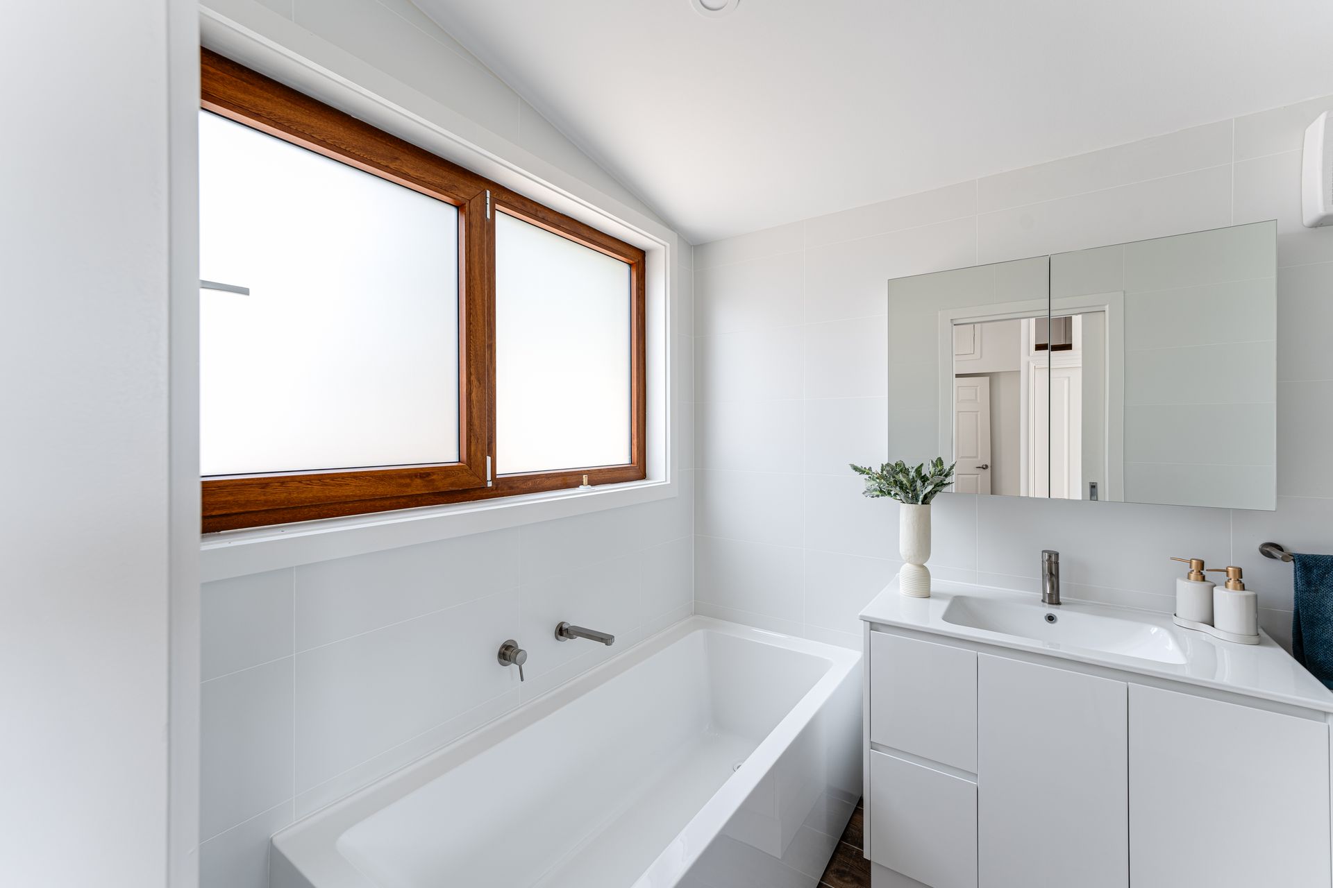 White bathroom with a bathtub, sink, and window.