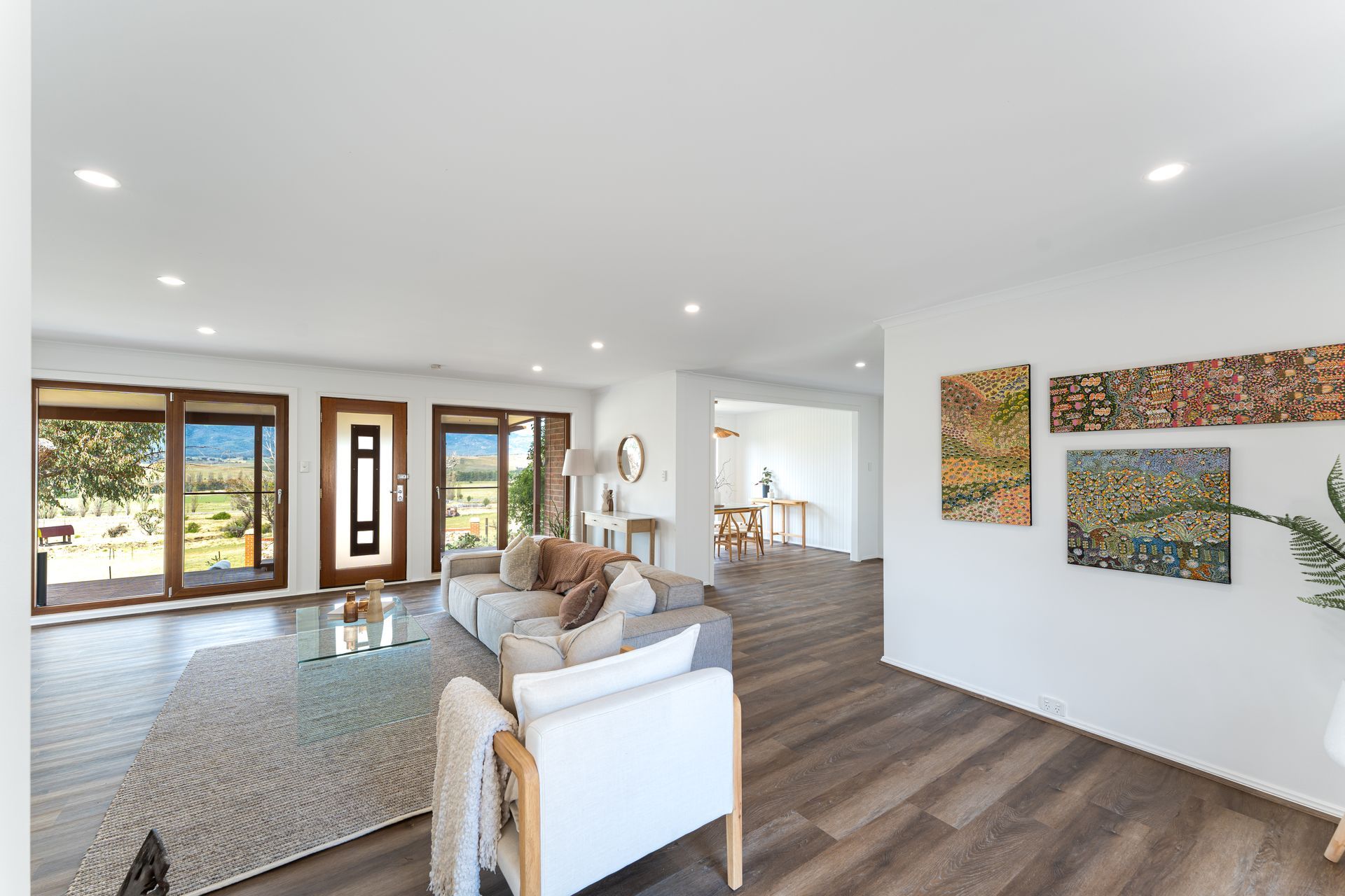 Bright living room with gray sofa, wood floors, sliding glass doors to outdoor view. Artwork on wall.