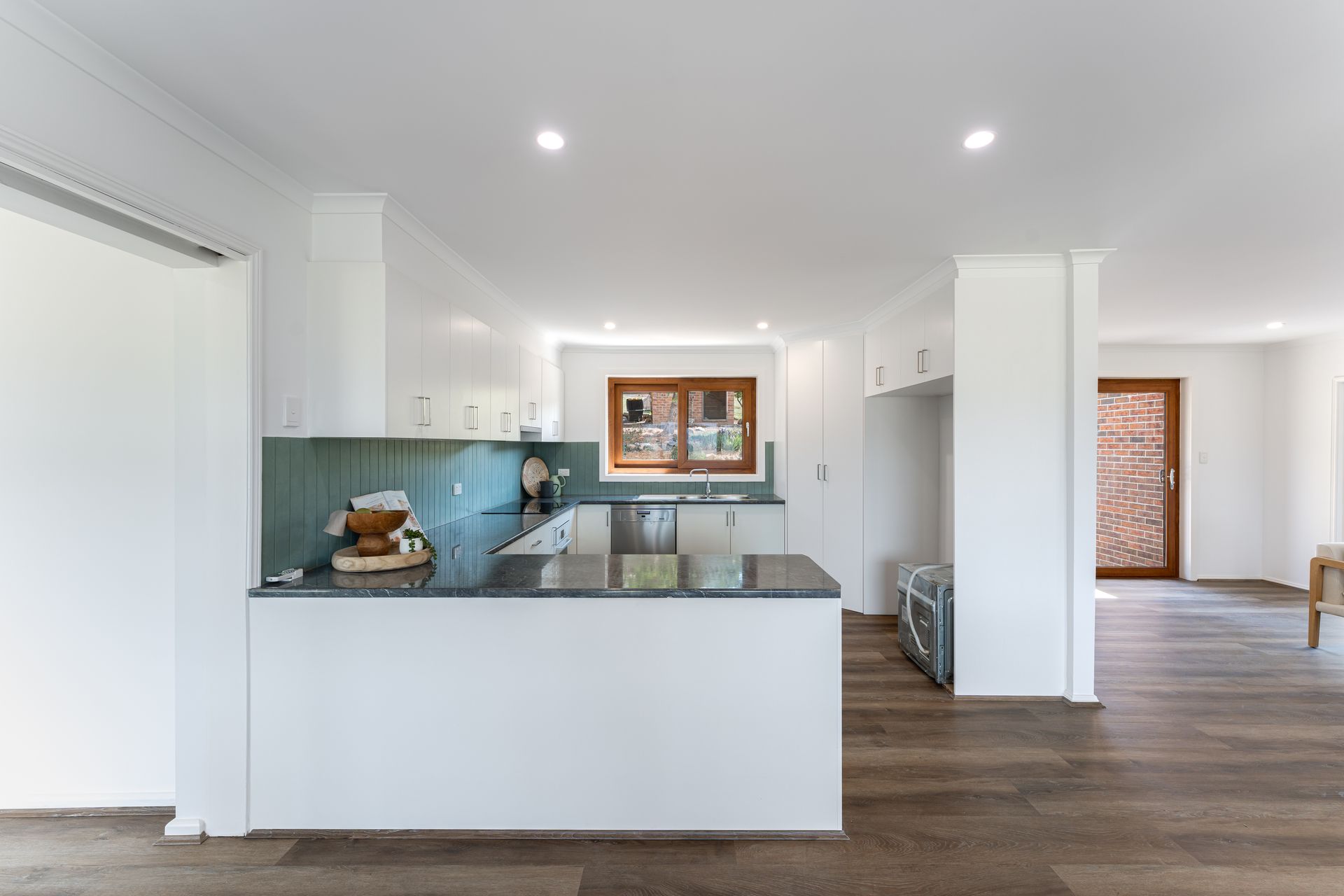Bright, open kitchen with white cabinets, dark countertops, teal backsplash, and dark wood flooring.