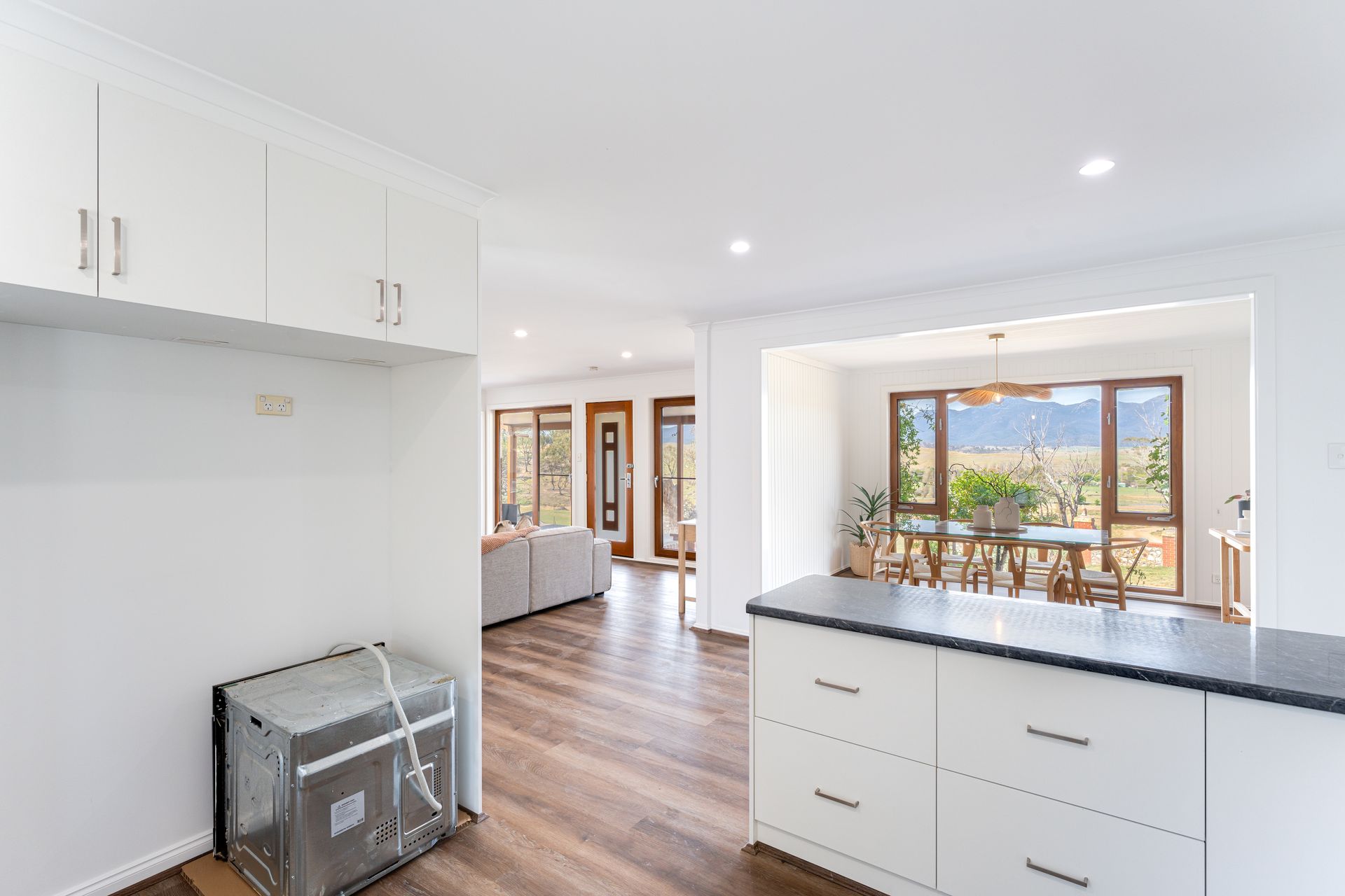 Bright kitchen with white cabinets, dark countertop, and view into the living and dining areas.