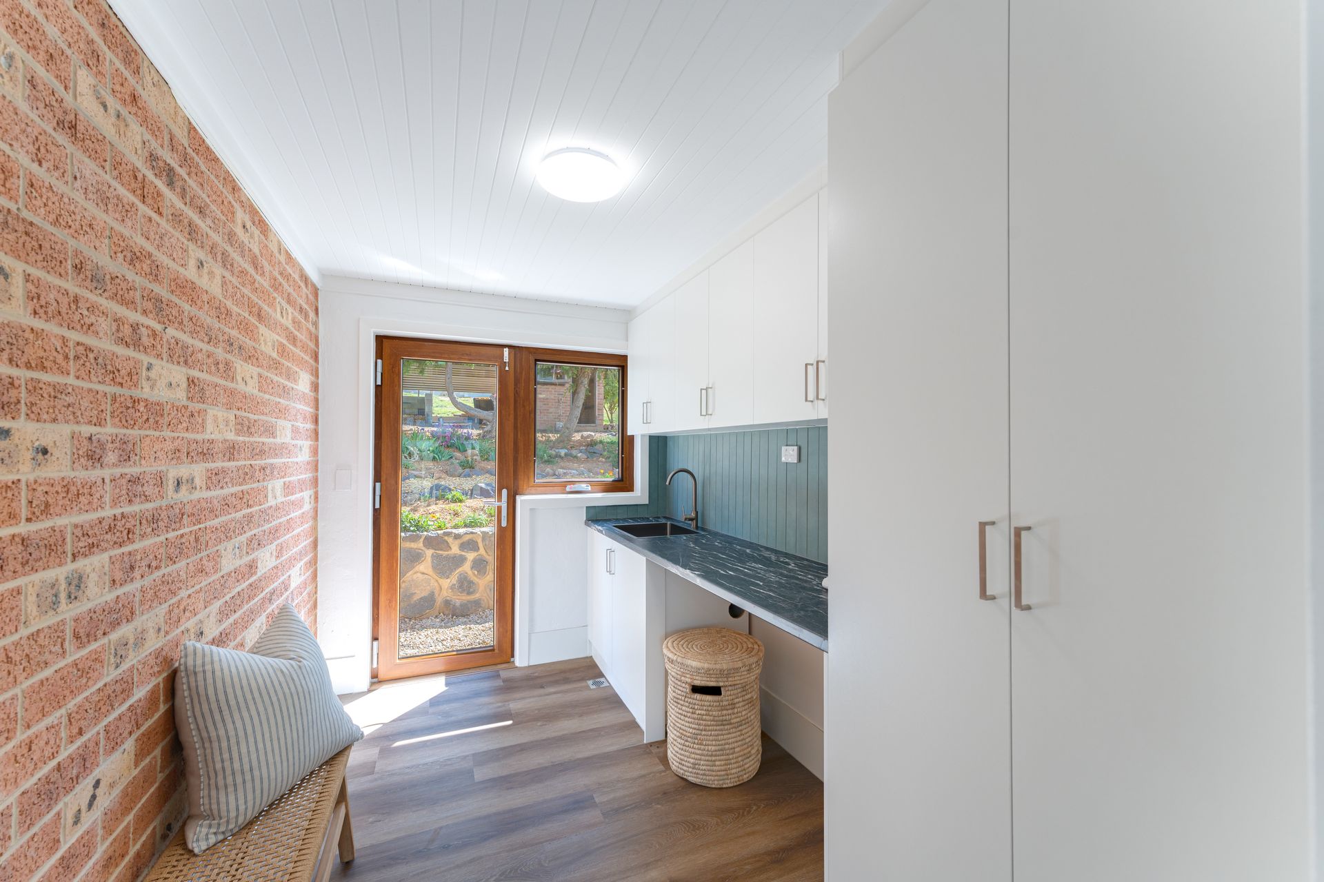 Laundry room with brick wall, white cabinets, sink, and wooden doors leading outside.