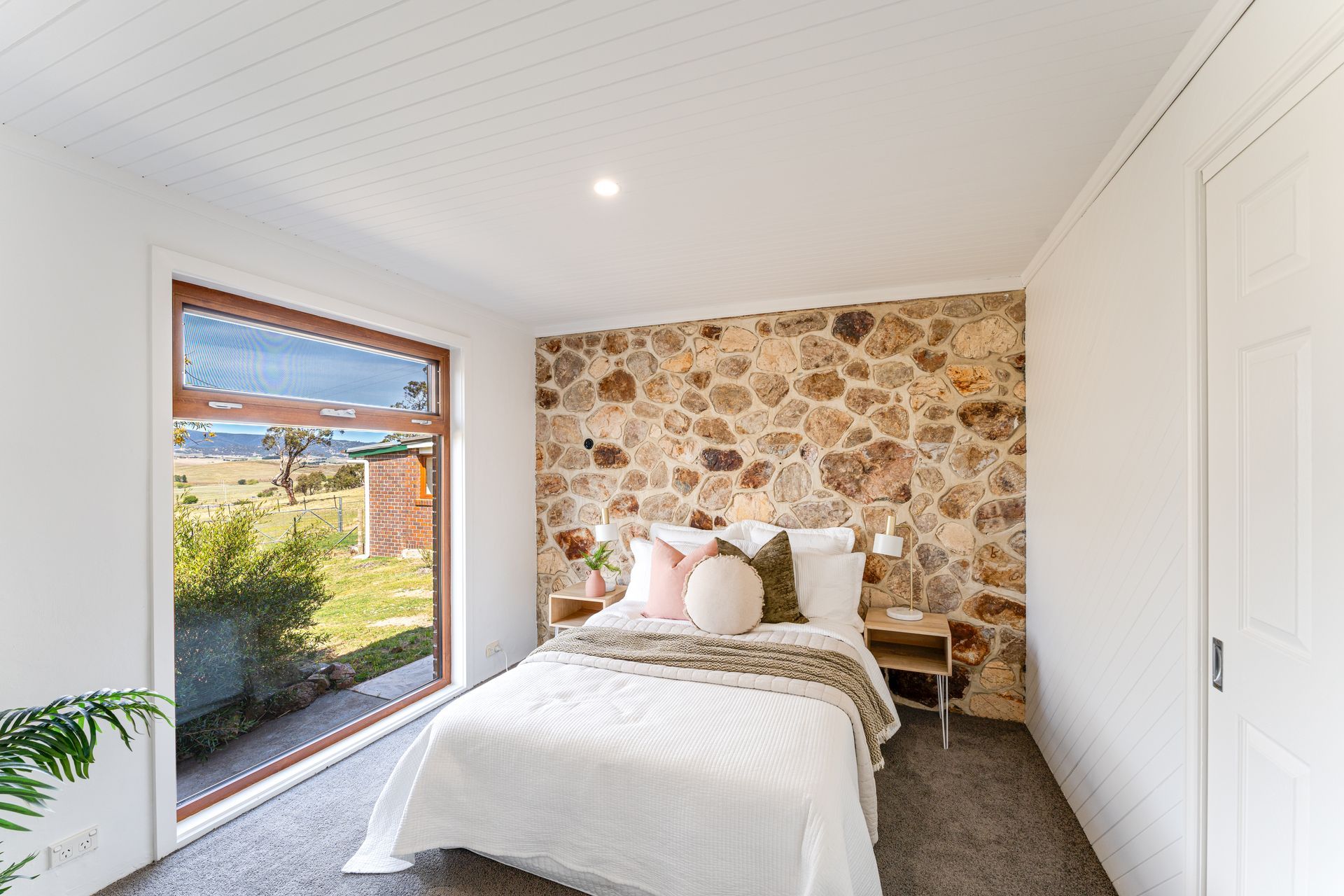 Bedroom with gray walls, bed with pillows, nightstands, and window with a shade.