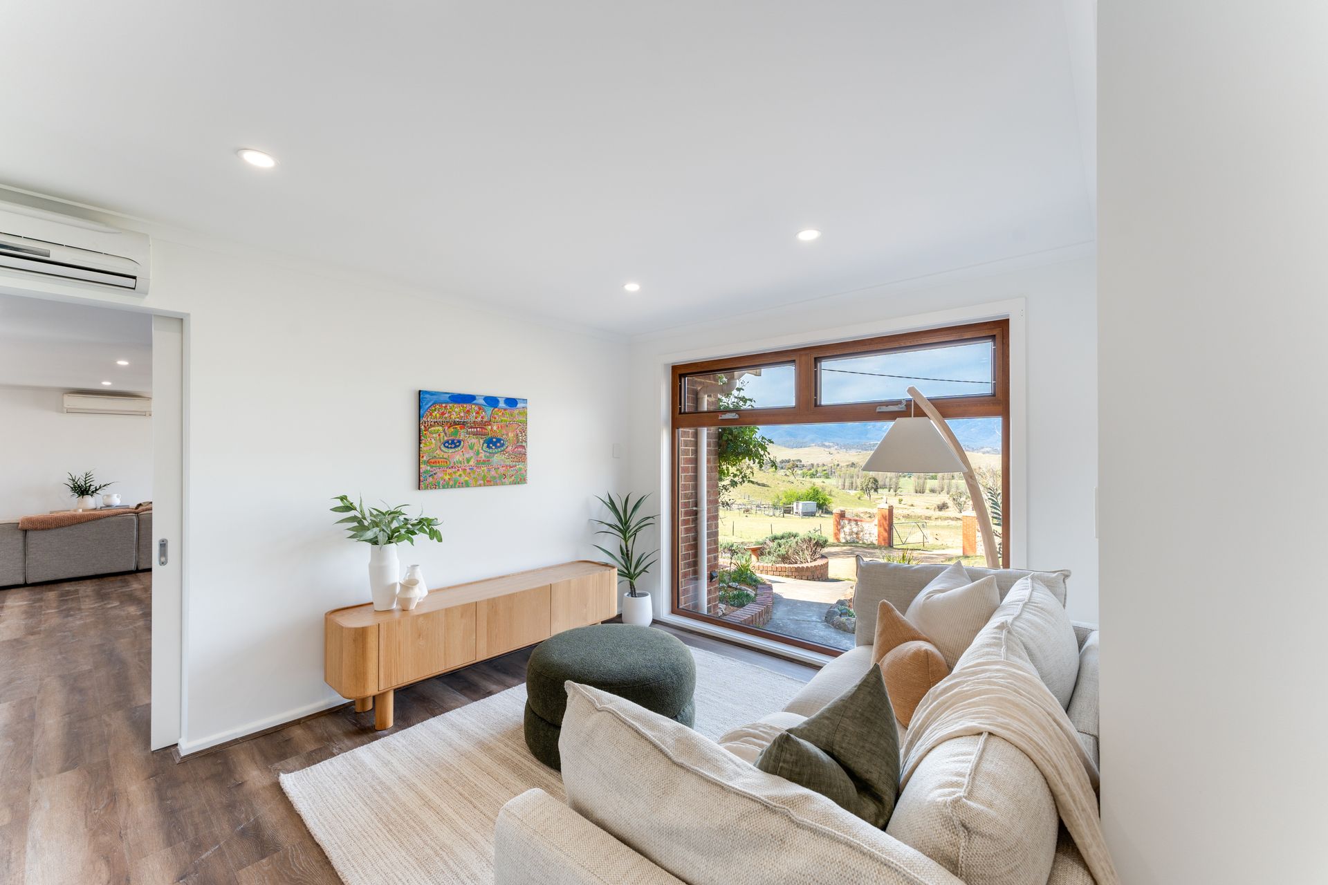 Living room with window overlooking landscape; light wood floors, neutral tones, modern decor.