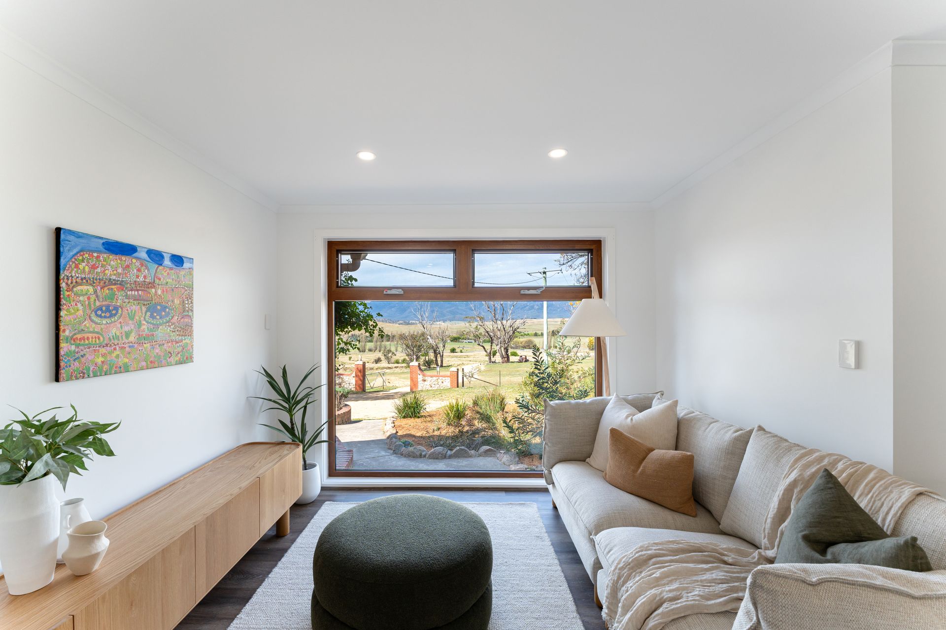 Living room with sofa, artwork, and large window overlooking a landscape.