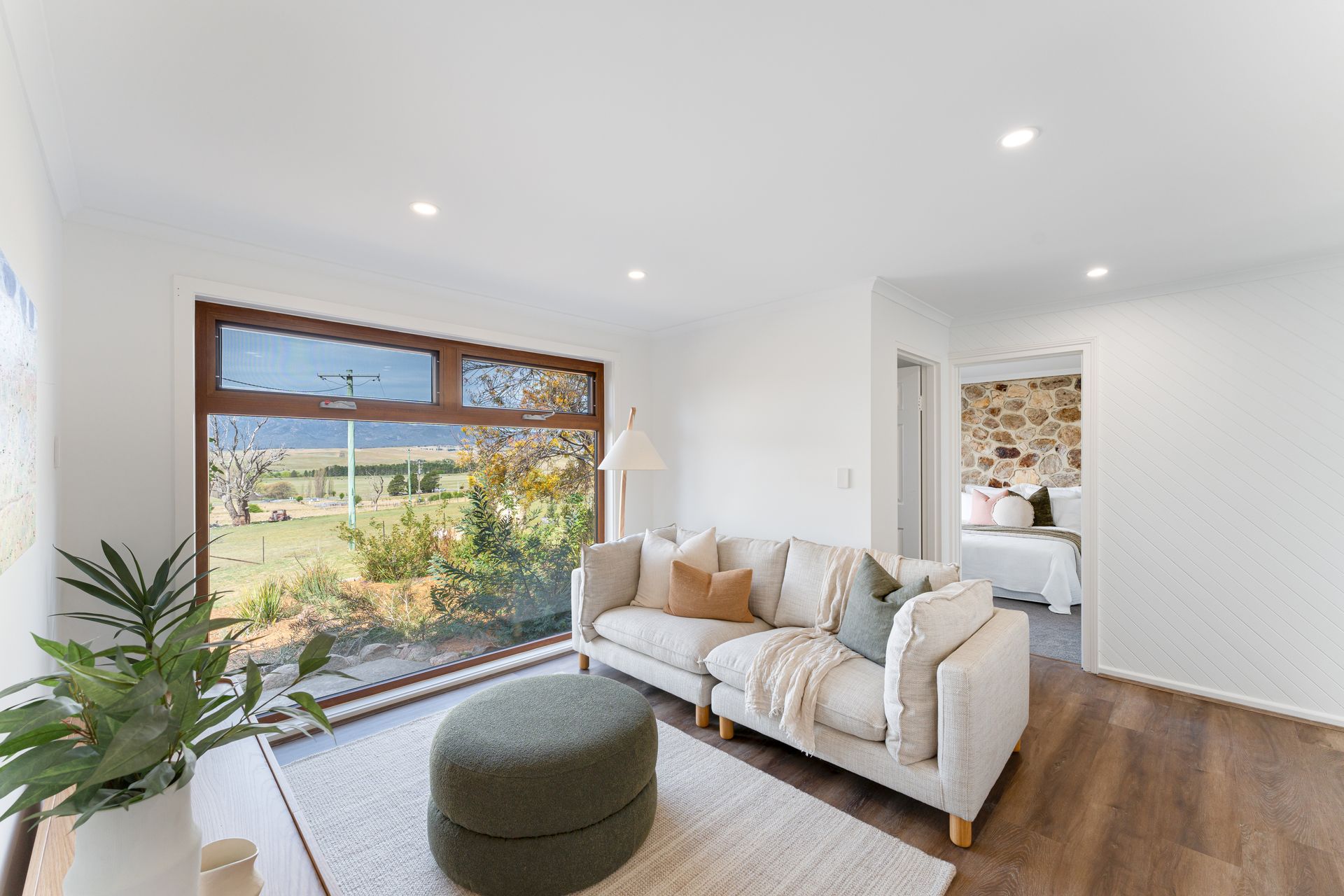 Living room with a white couch, ottoman, large window overlooking a yard.