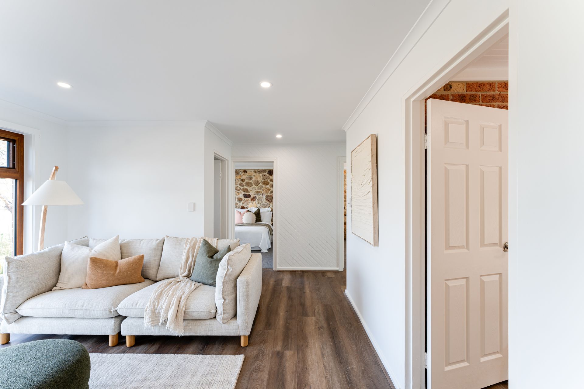 Living room with a light-colored sectional sofa, wooden floors, and a view into a bedroom and doorway.