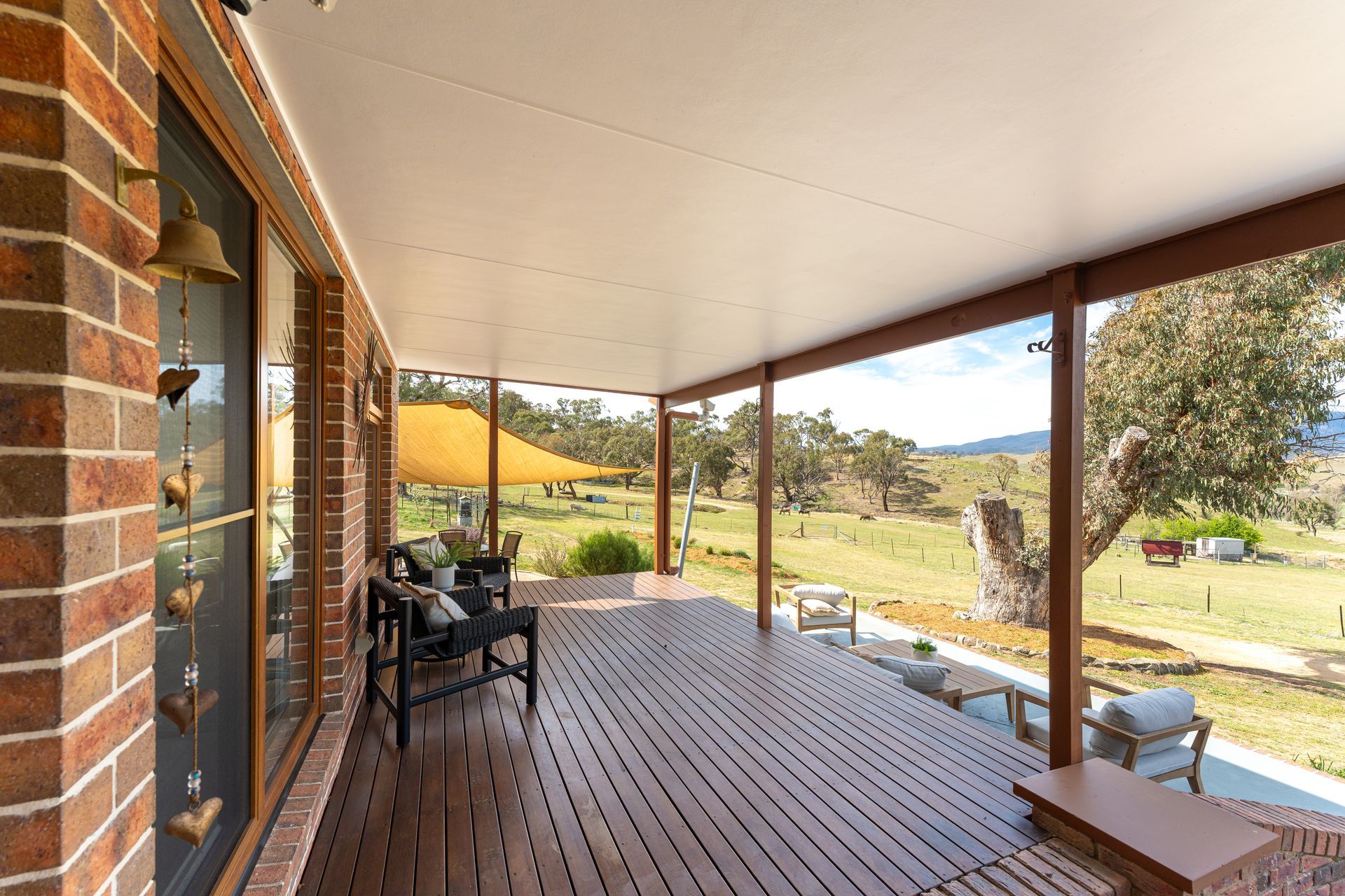 Covered porch with wood flooring, overlooking a green field and trees.