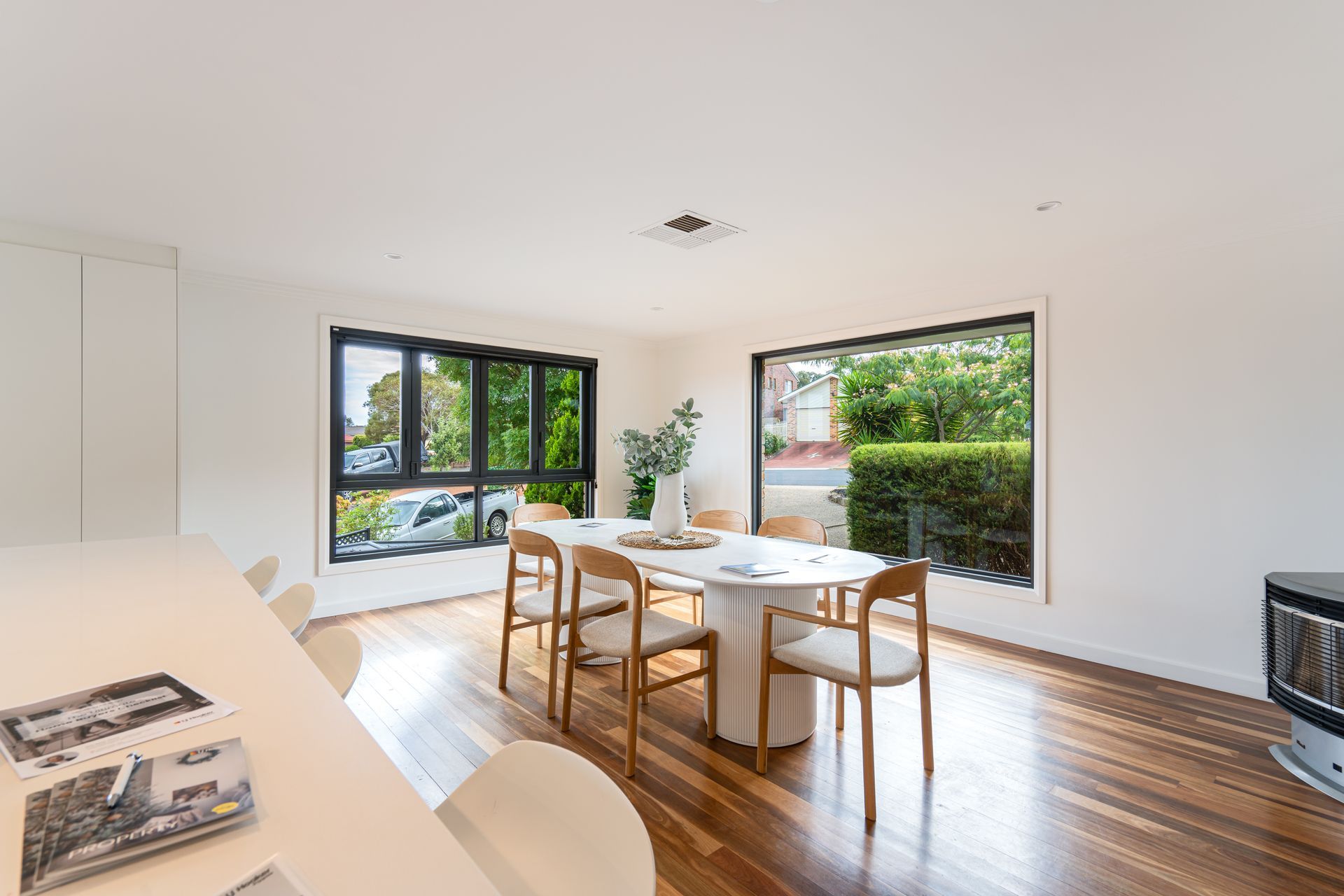 Dining room with a white table, wooden chairs, and large windows with outdoor views.