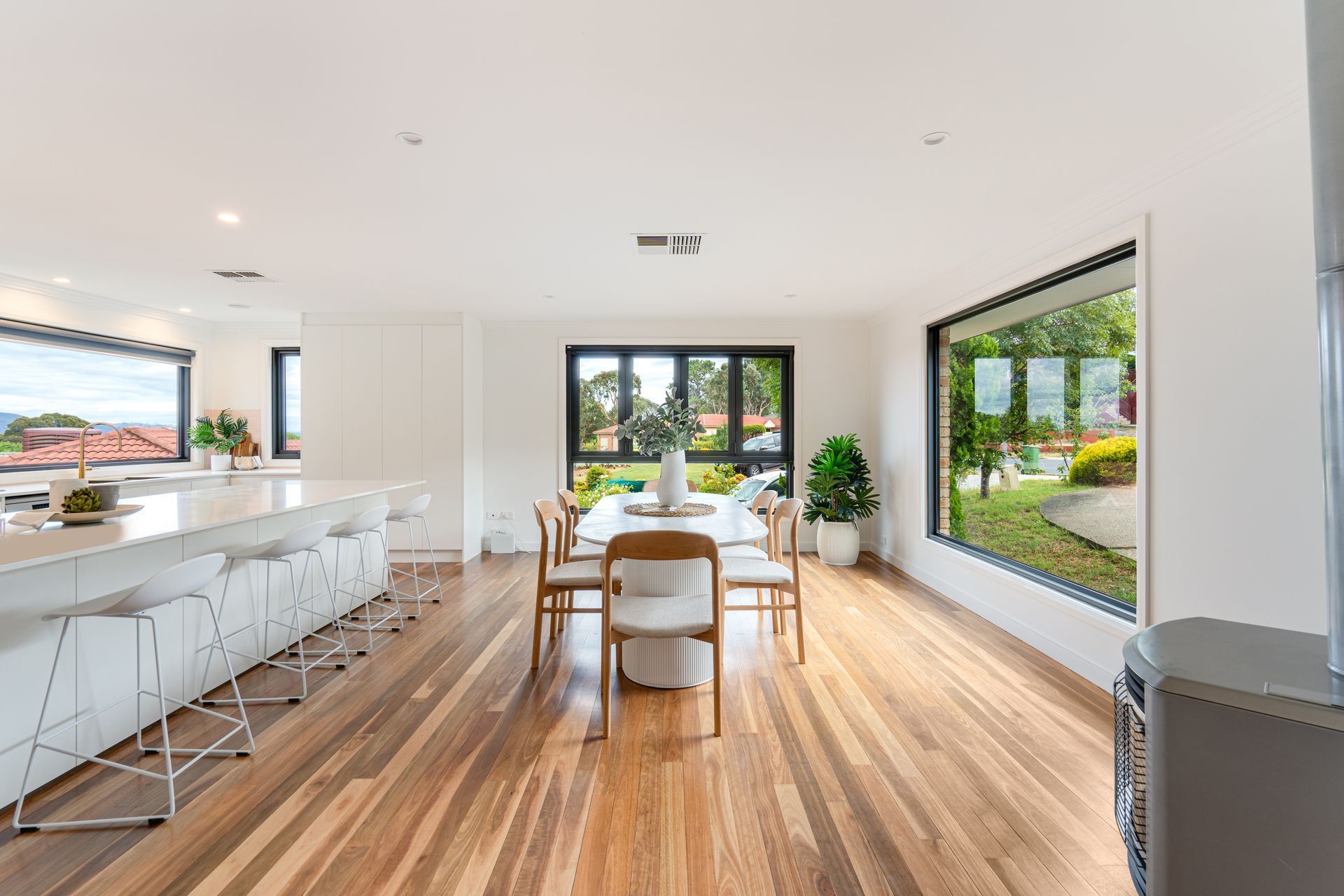 Bright open-plan dining area with a long white kitchen island, wooden floors, and a table set for dining, with a large window.