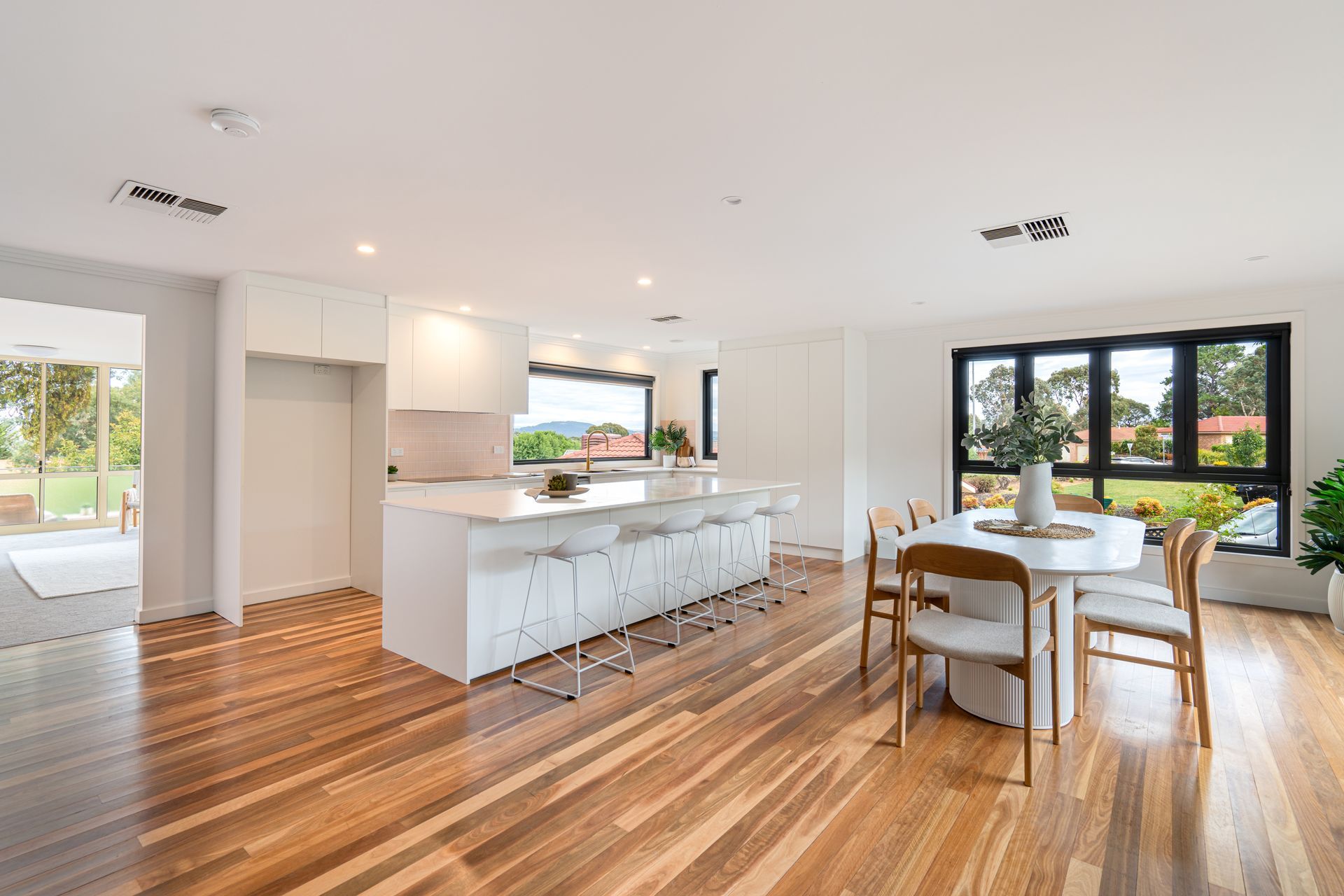 Bright, modern kitchen and dining area with white cabinets, island, wooden floors, and large windows.