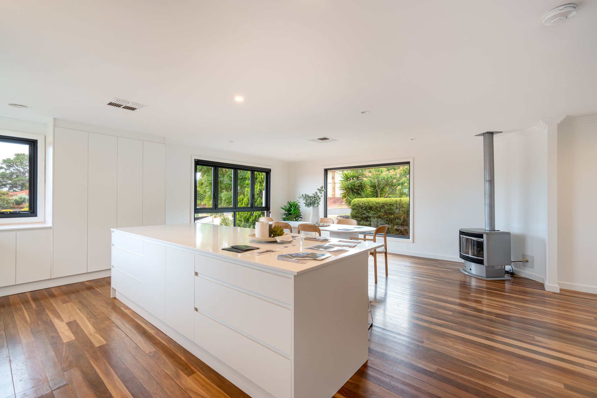 Modern kitchen with white island, hardwood floors, large windows, and a wood-burning stove.