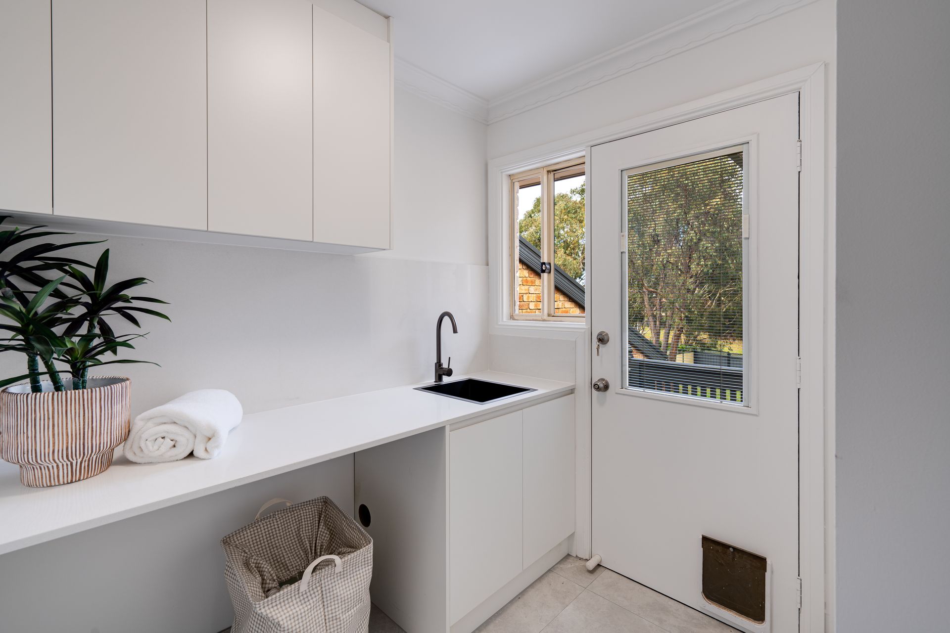 White laundry room with cabinets, counter, window, and shelves.