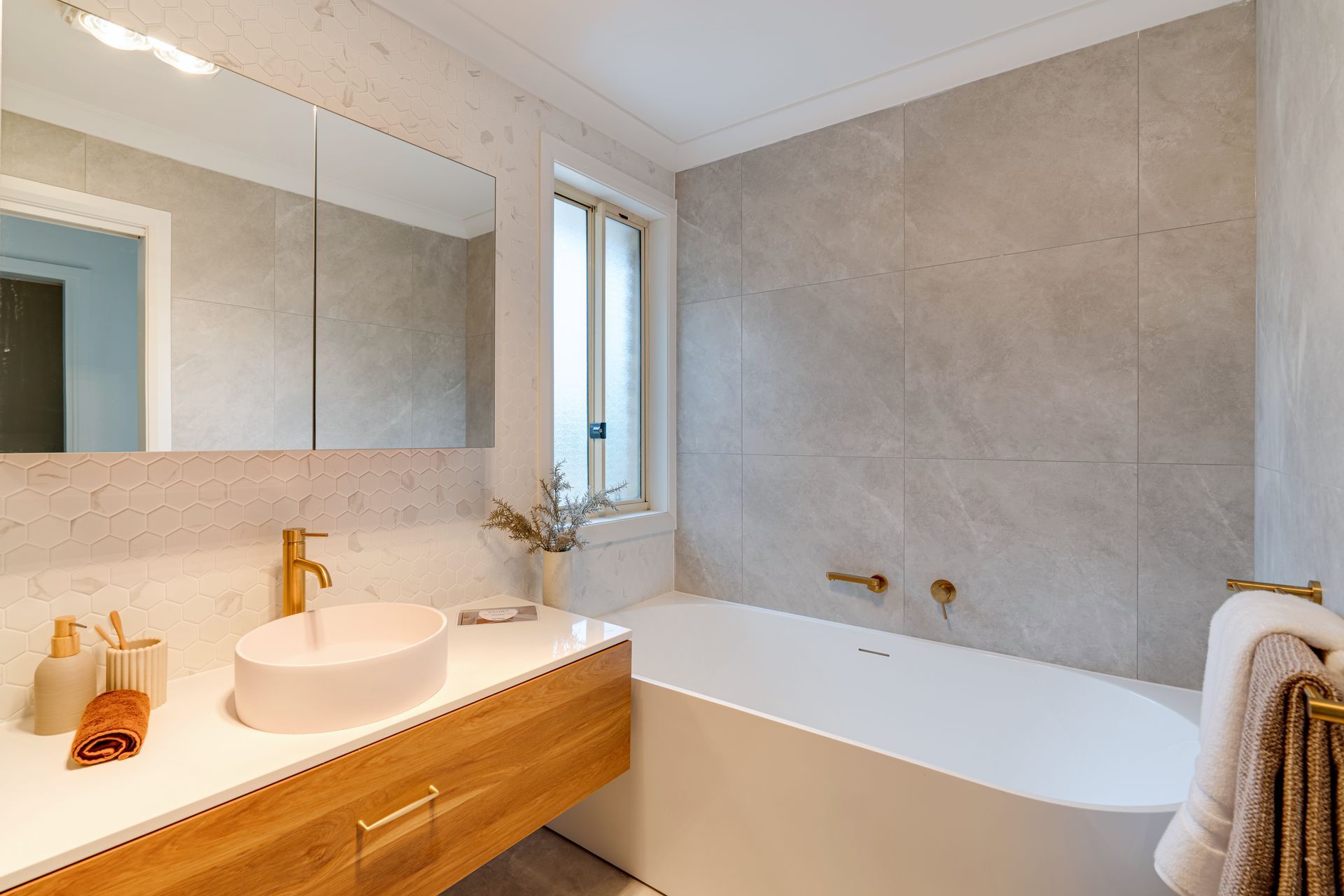 Bathroom with wooden vanity, oval sink, freestanding tub, and gray tile walls.