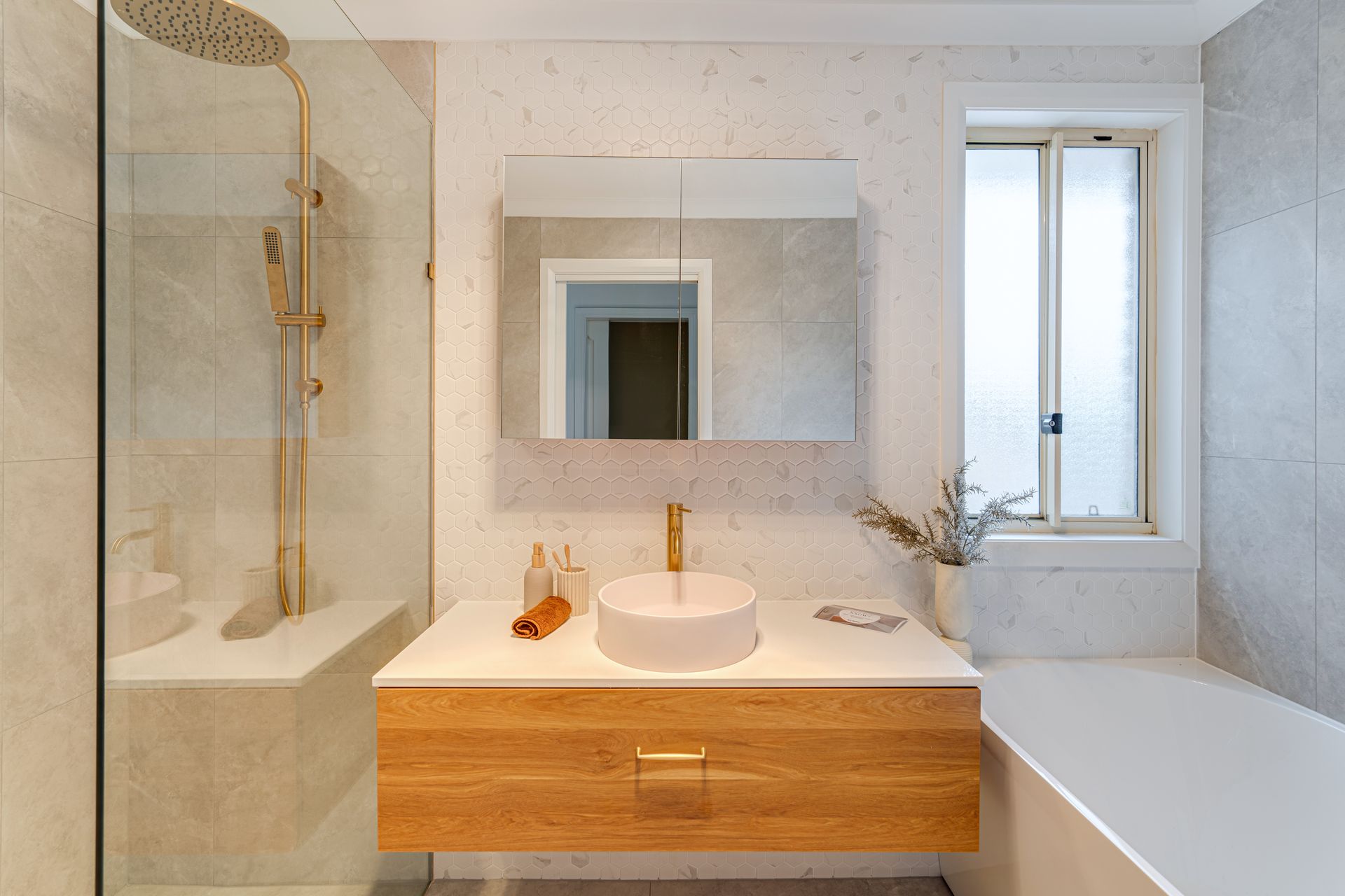 Modern bathroom with a wooden vanity, round sink, gold faucet, and glass shower.