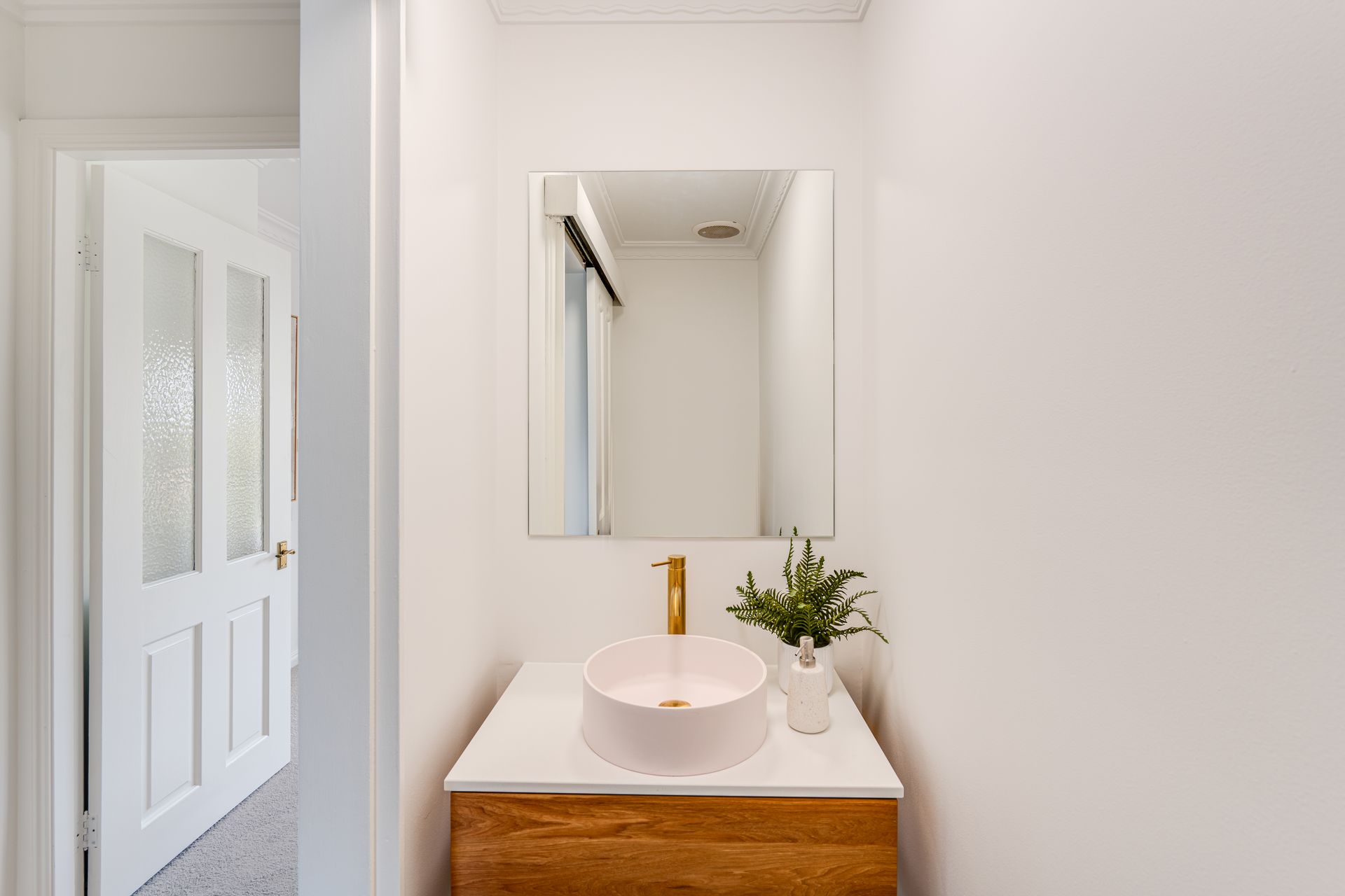 White laundry room with sink, counter, cabinets, and door to outside. Plant and laundry basket are present.