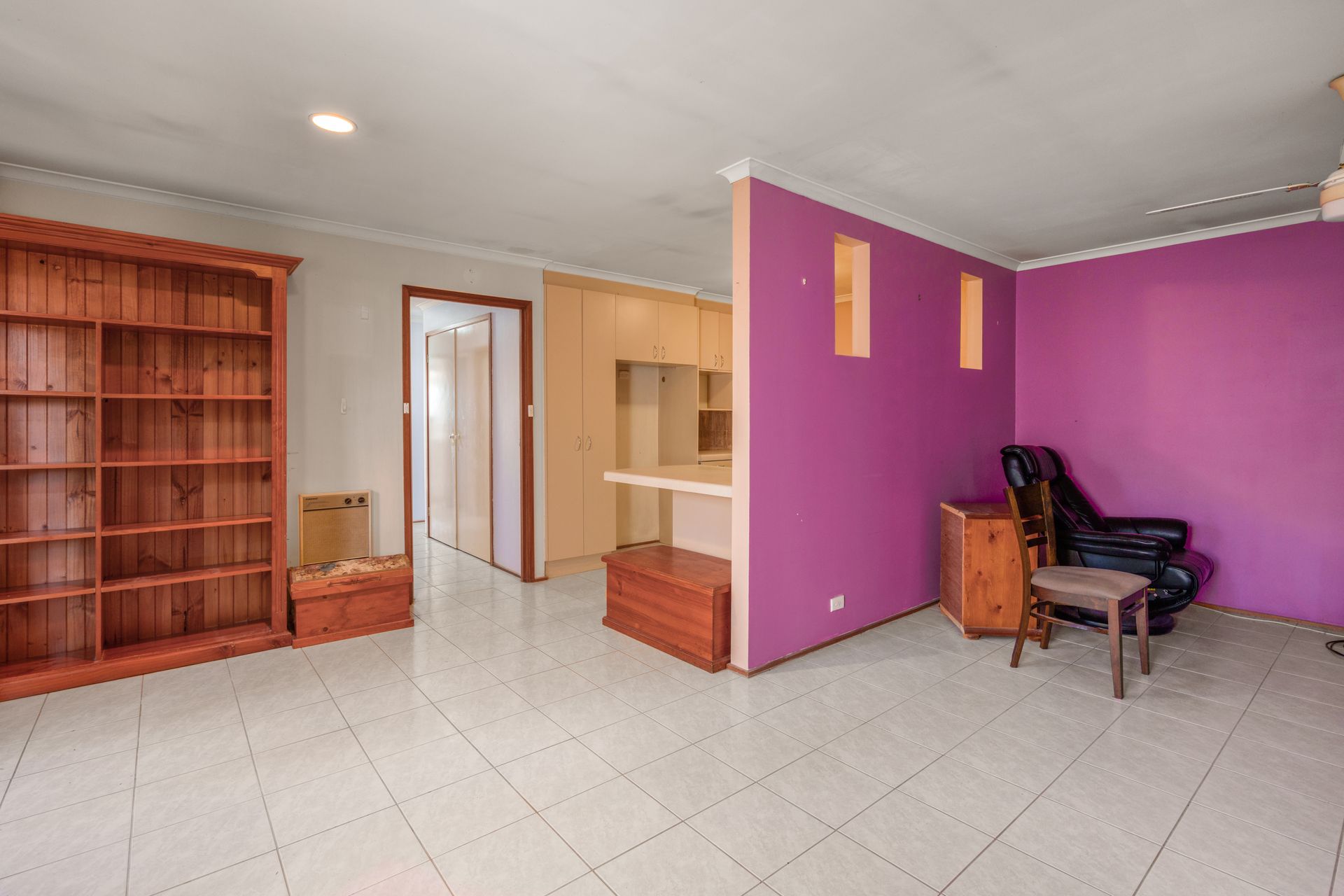 Bedroom with bed, stacked cushions, window, and small cabinet.