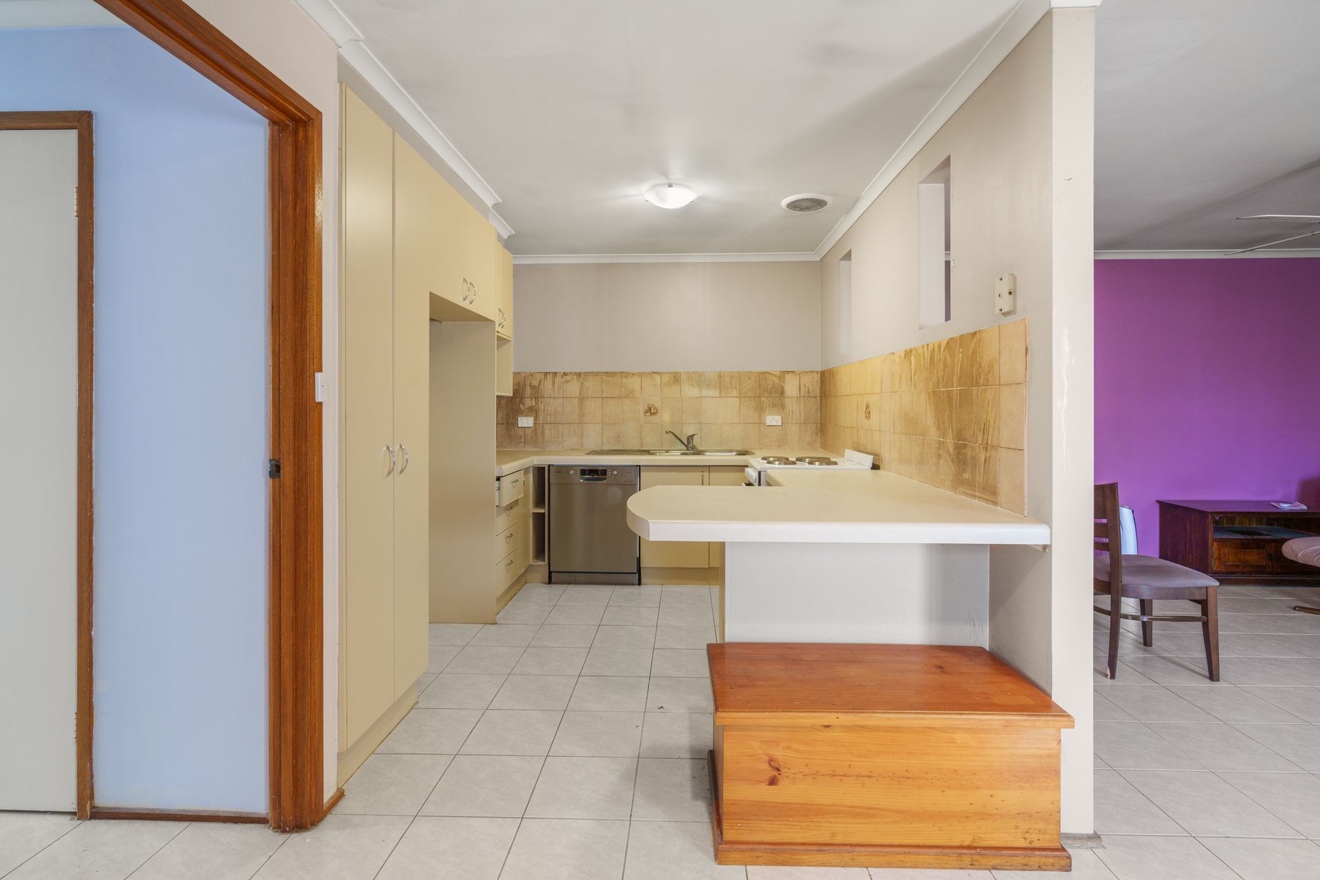 Backyard patio with brick wall, overhead shelter, chairs, and overgrown weeds.