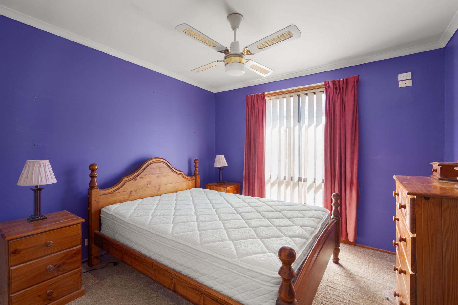 Bedroom with purple walls, wooden bed frame, mattress, nightstands, curtains, ceiling fan, and dresser.