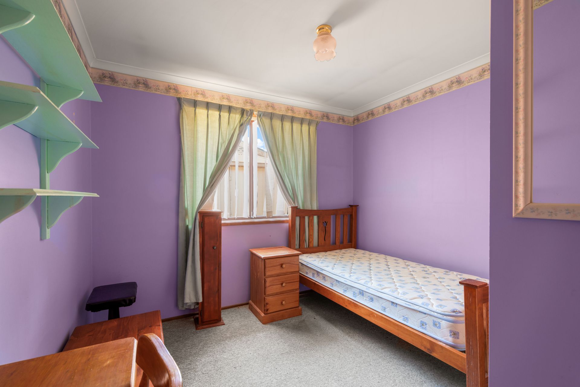 Bedroom with bed, stacked cushions, window, and small cabinet.