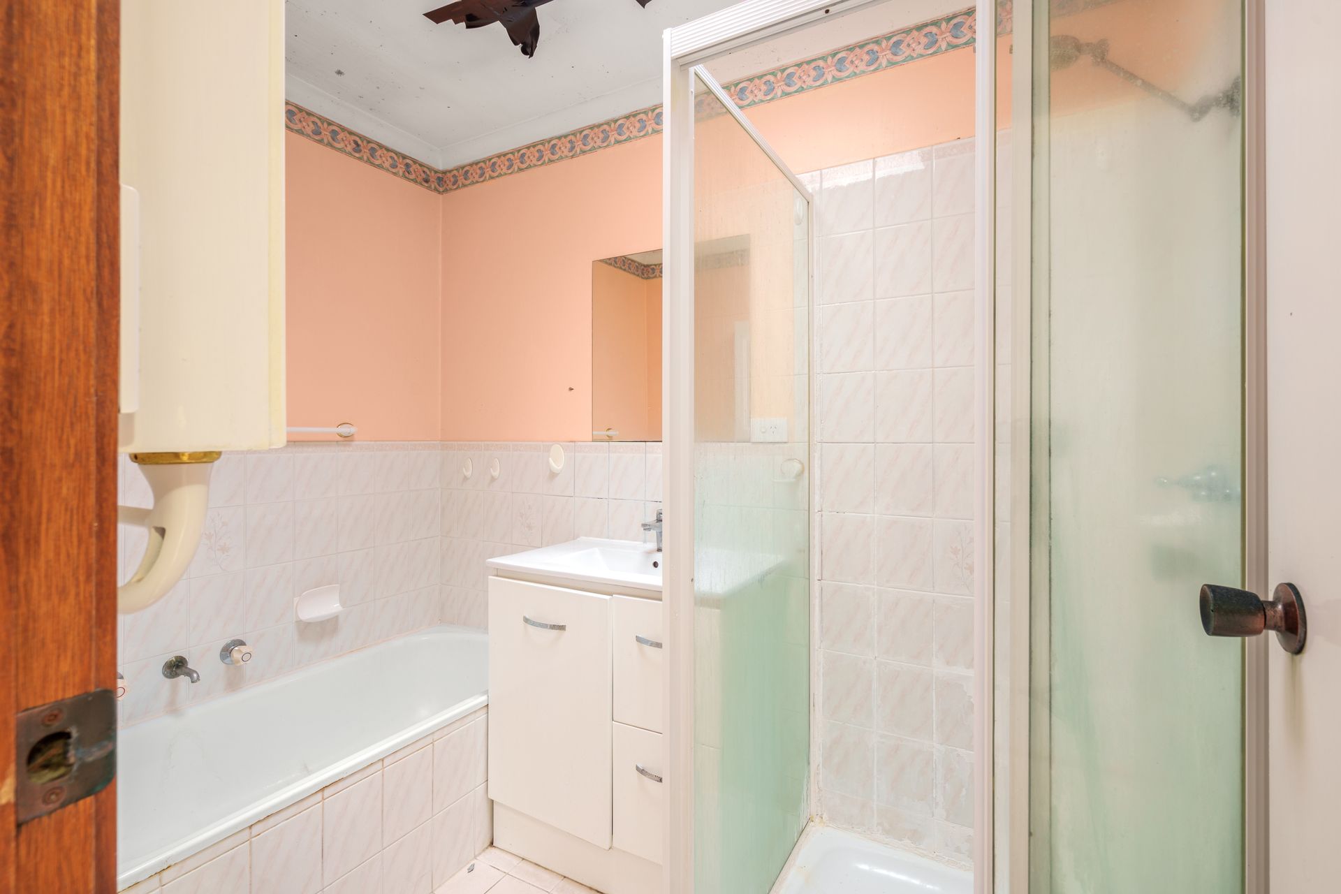 Bathroom with a tub, shower, sink, and mirror. White and peach colored walls, wood door frame.
