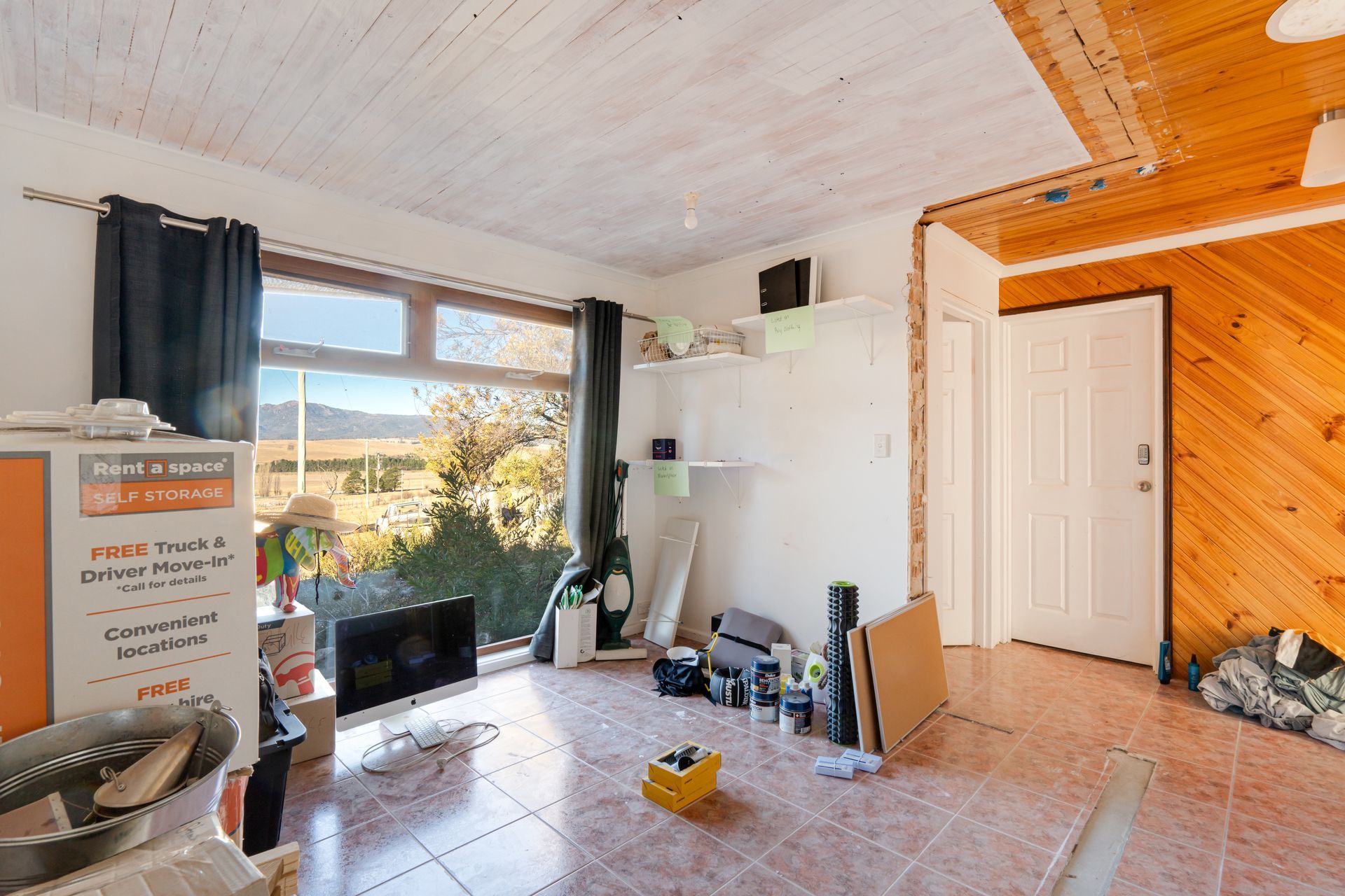 Bedroom with bed, stacked cushions, window, and small cabinet.