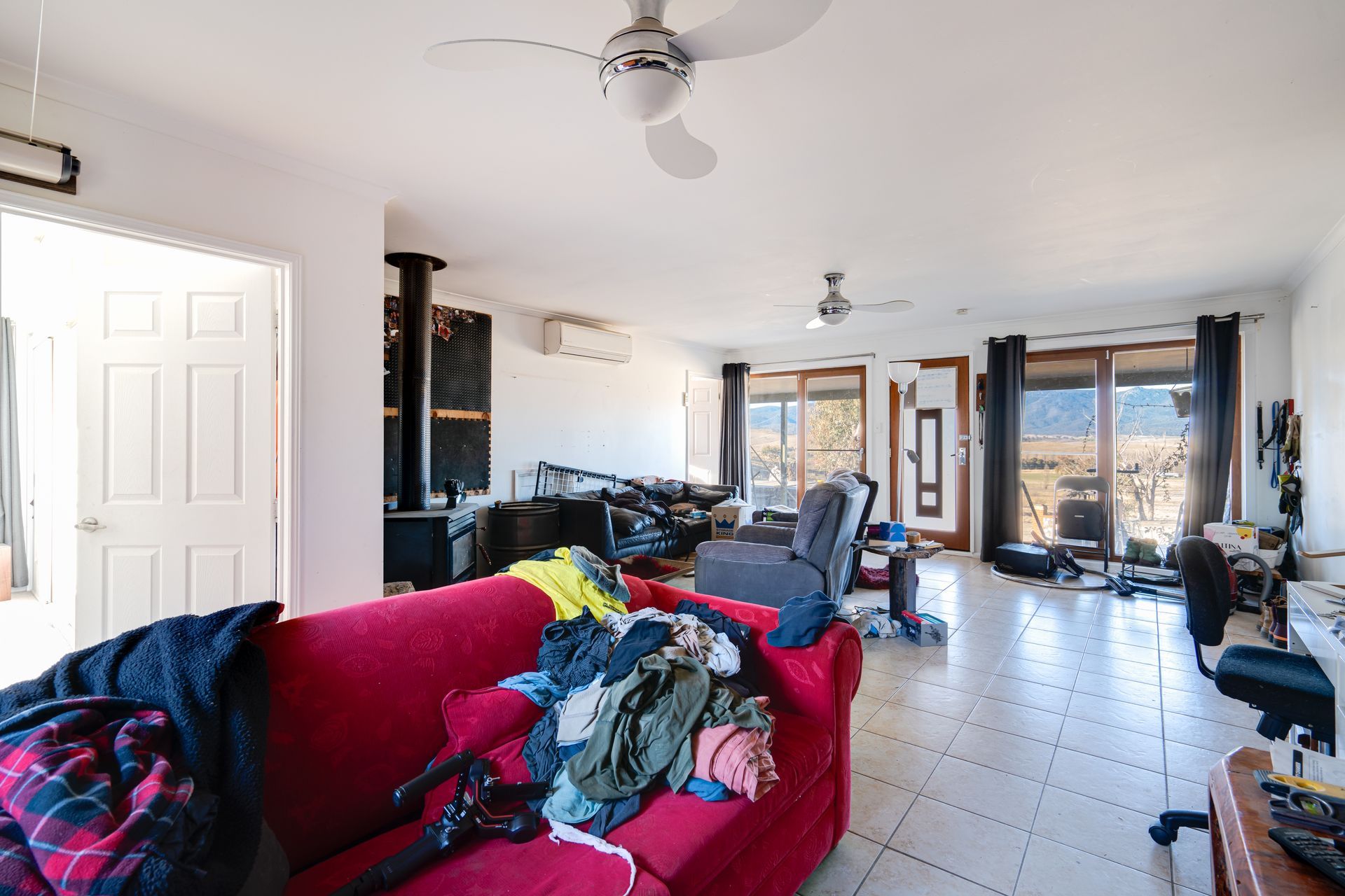 Messy living room with a red couch, a door, and a view of mountains.