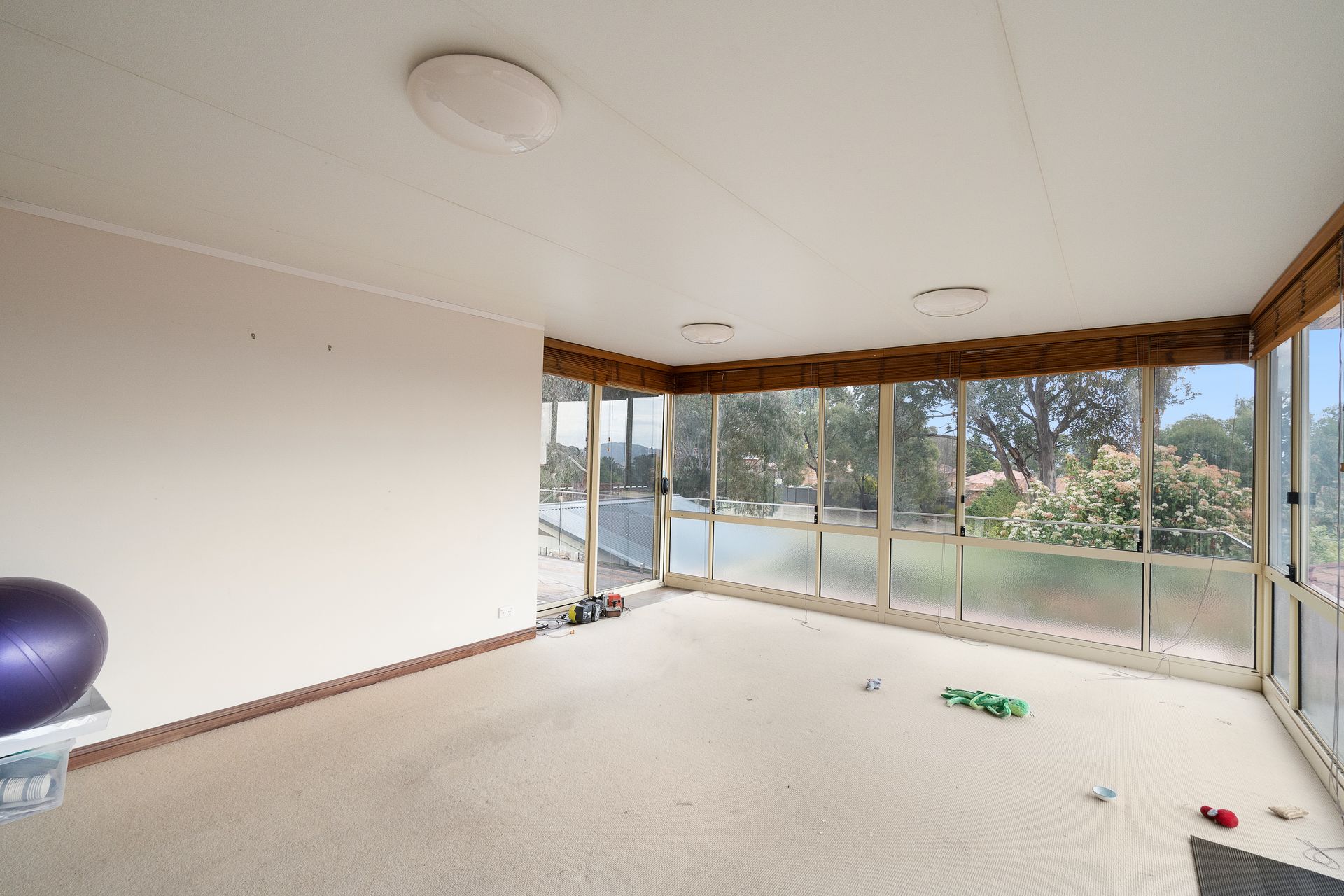 Bedroom with bed, stacked cushions, window, and small cabinet.