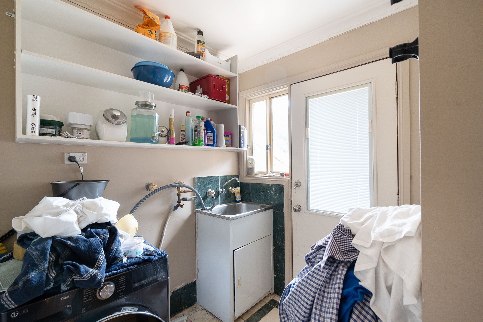 Bedroom with bed, stacked cushions, window, and small cabinet.