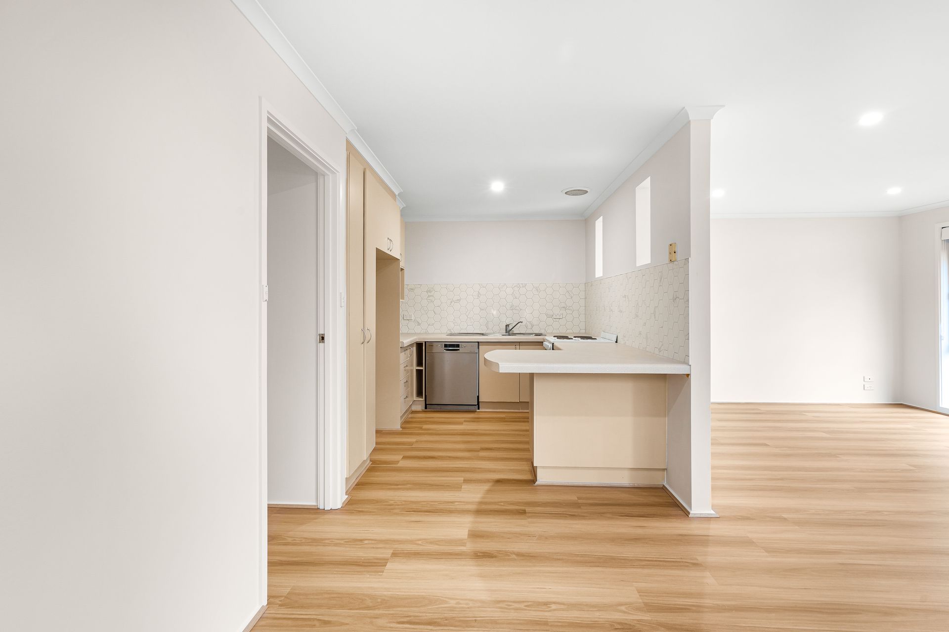 Empty, bright kitchen with light wooden floors, white walls, and a breakfast bar.