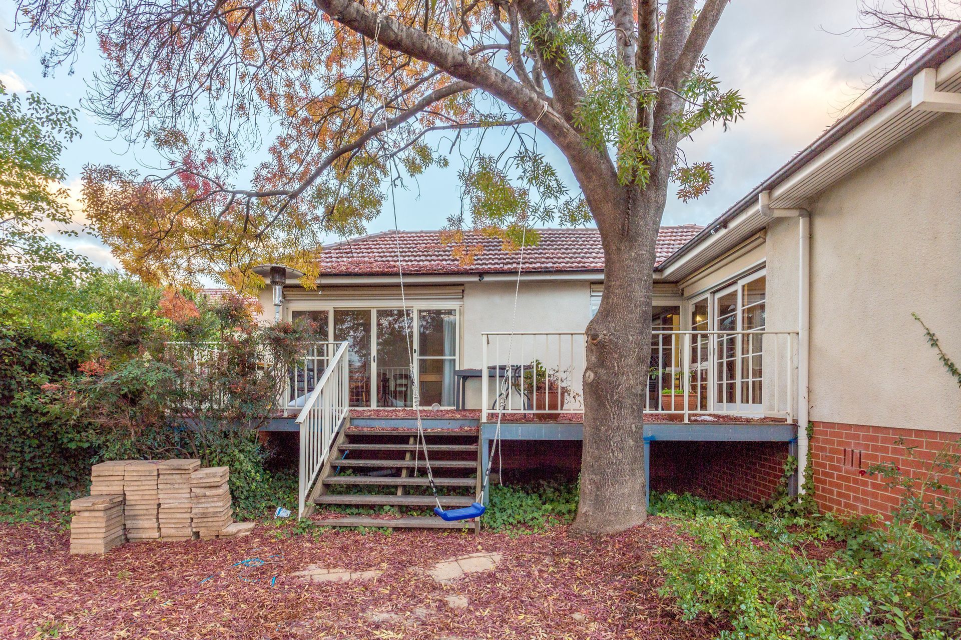 Backyard with deck and house. Large tree in front, red brick base. Autumn leaves.