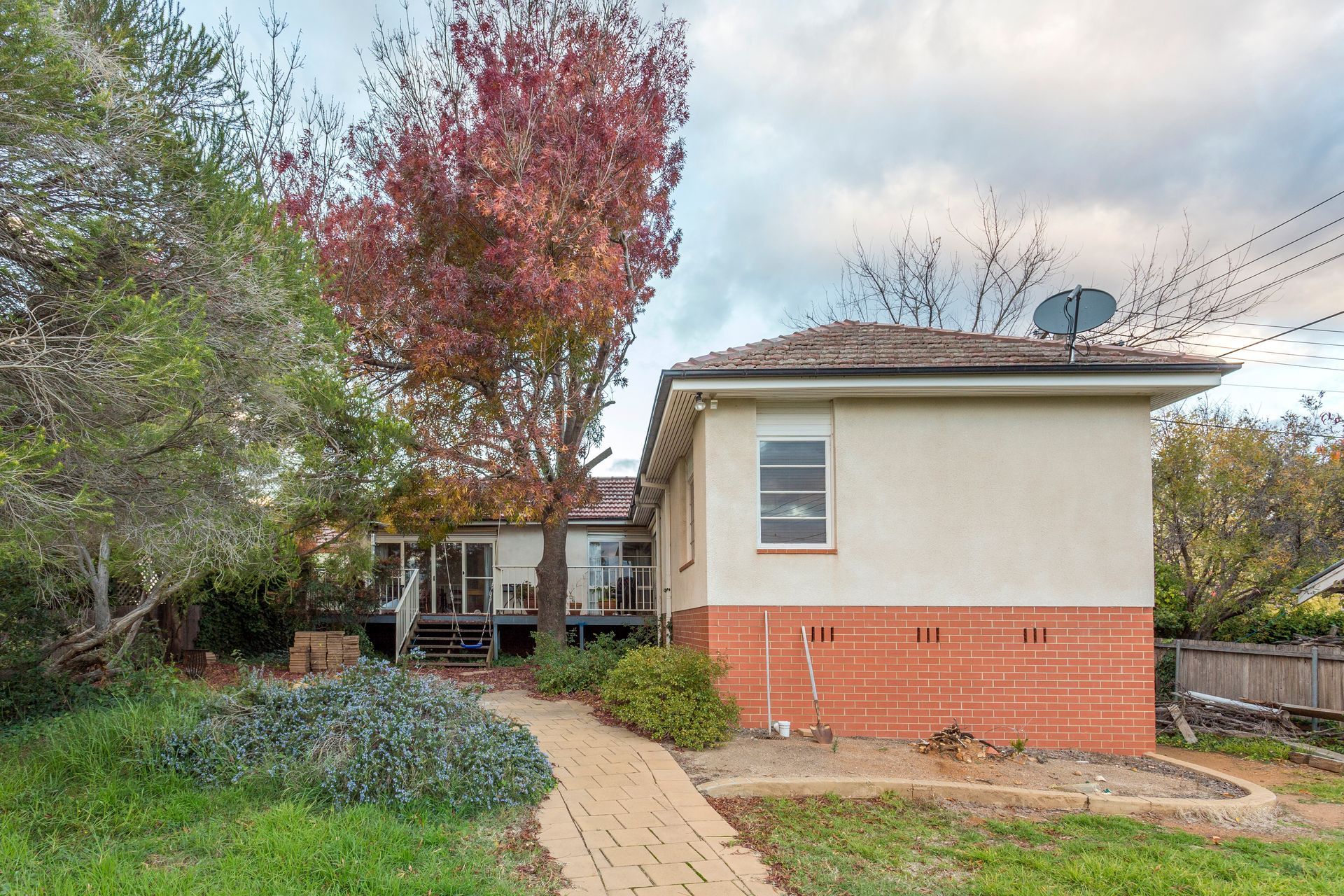 Backyard with deck and house. Large tree in front, red brick base. Autumn leaves.