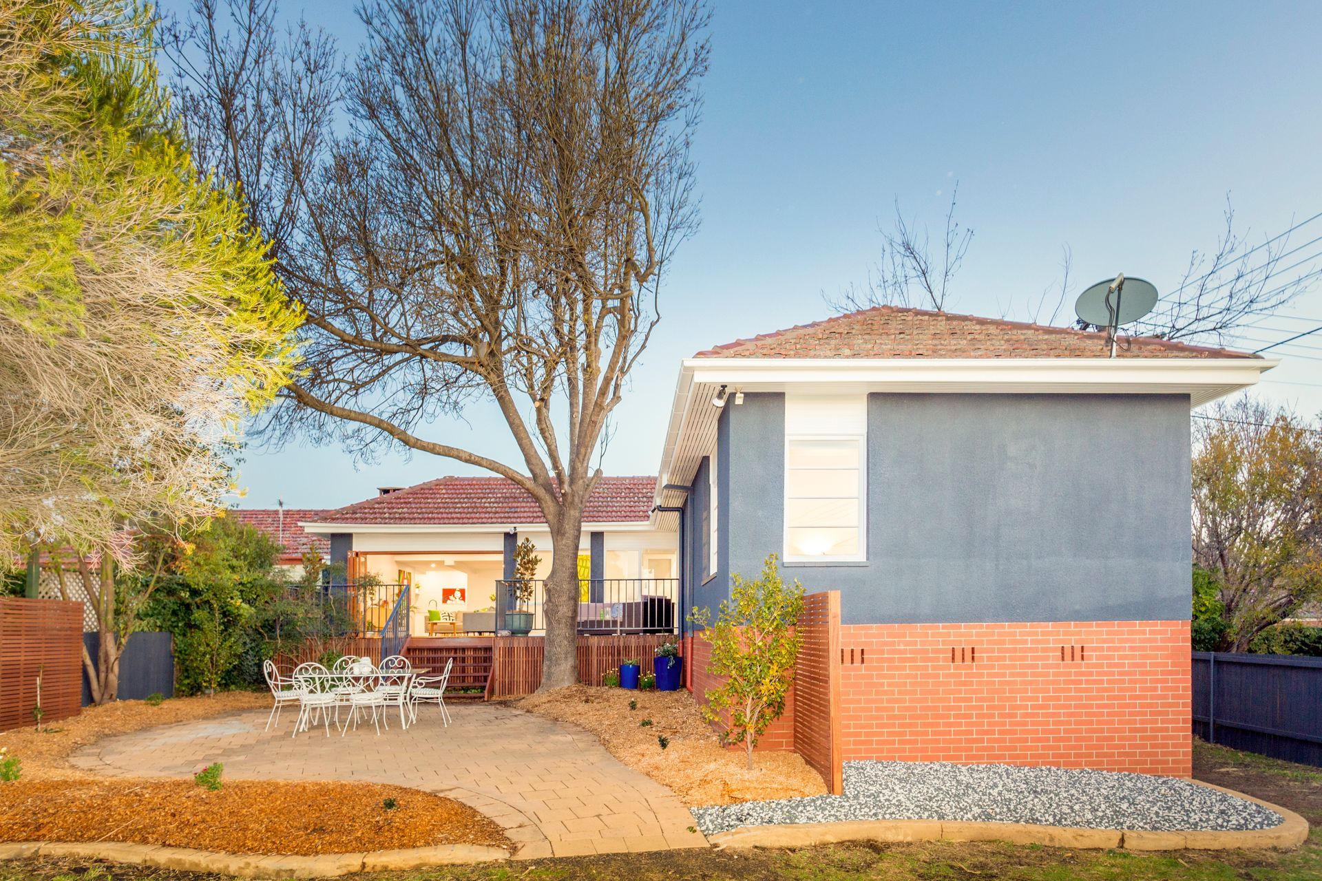 Backyard view of a house with a patio, brick foundation, and large tree.