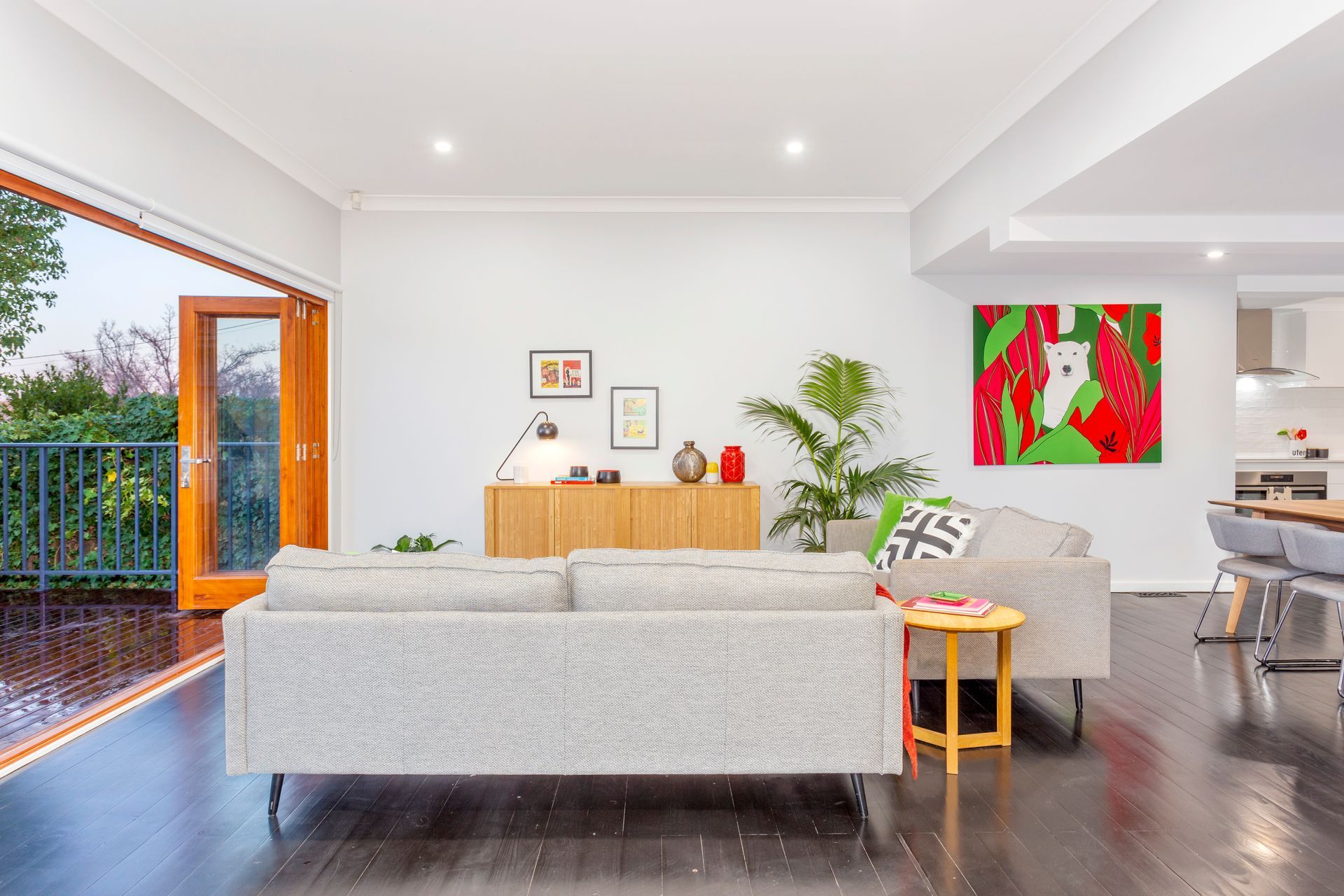 Living room with open doors to a balcony, light grey couches, and colorful artwork.
