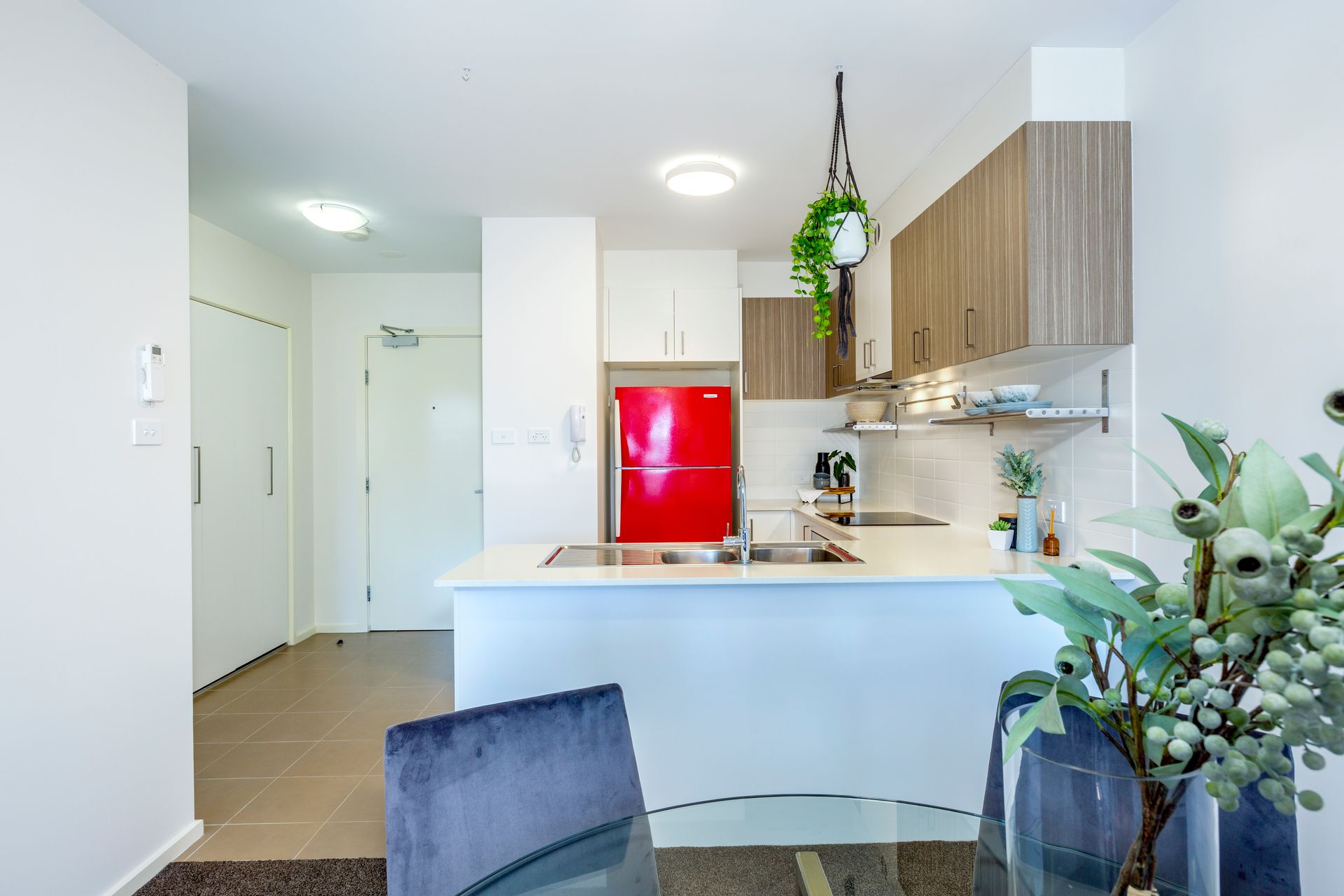 Modern kitchen with red refrigerator, white counters, and brown cabinets.