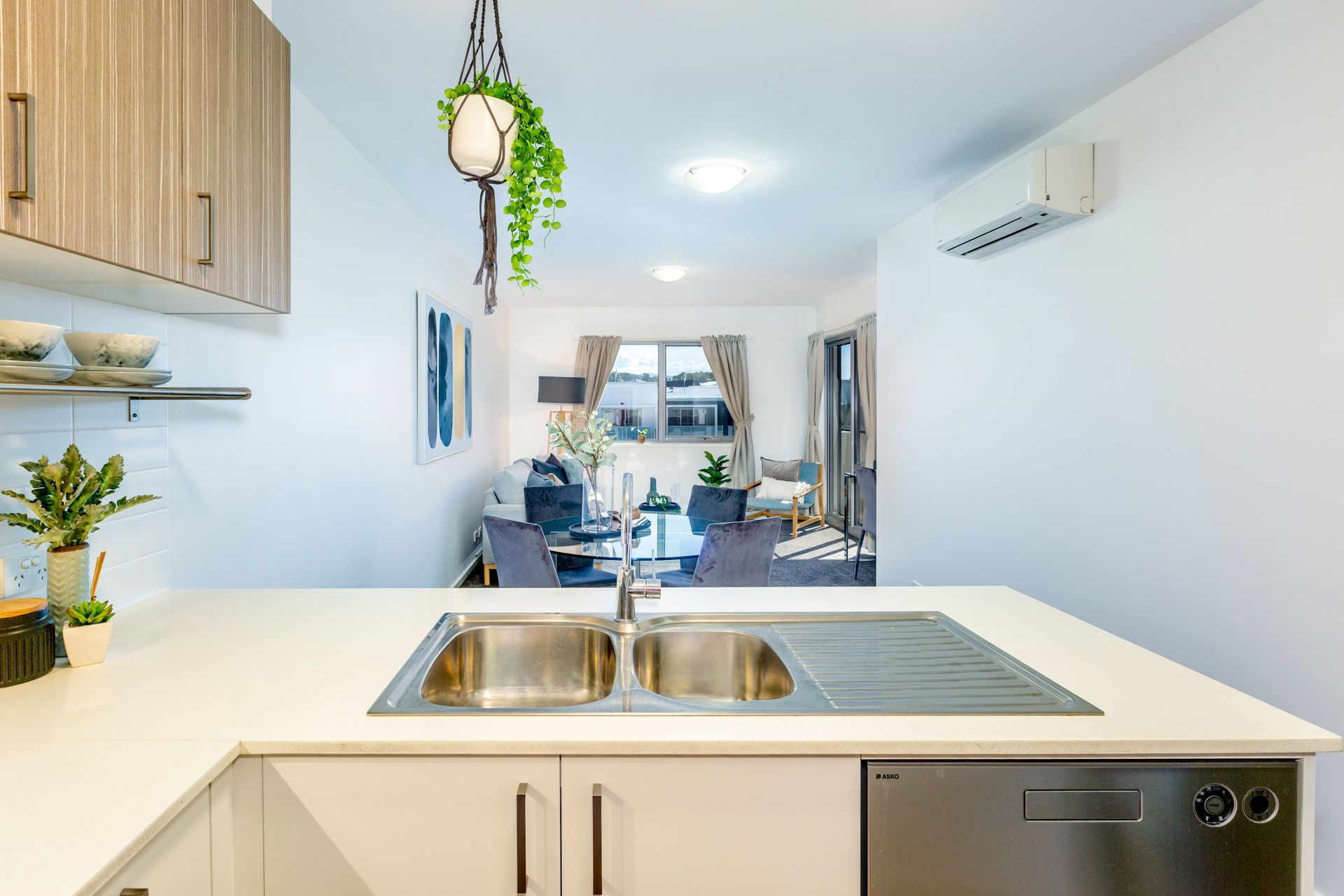 Kitchen with a white countertop, stainless steel sink, and a view into a living room with a couch and window.