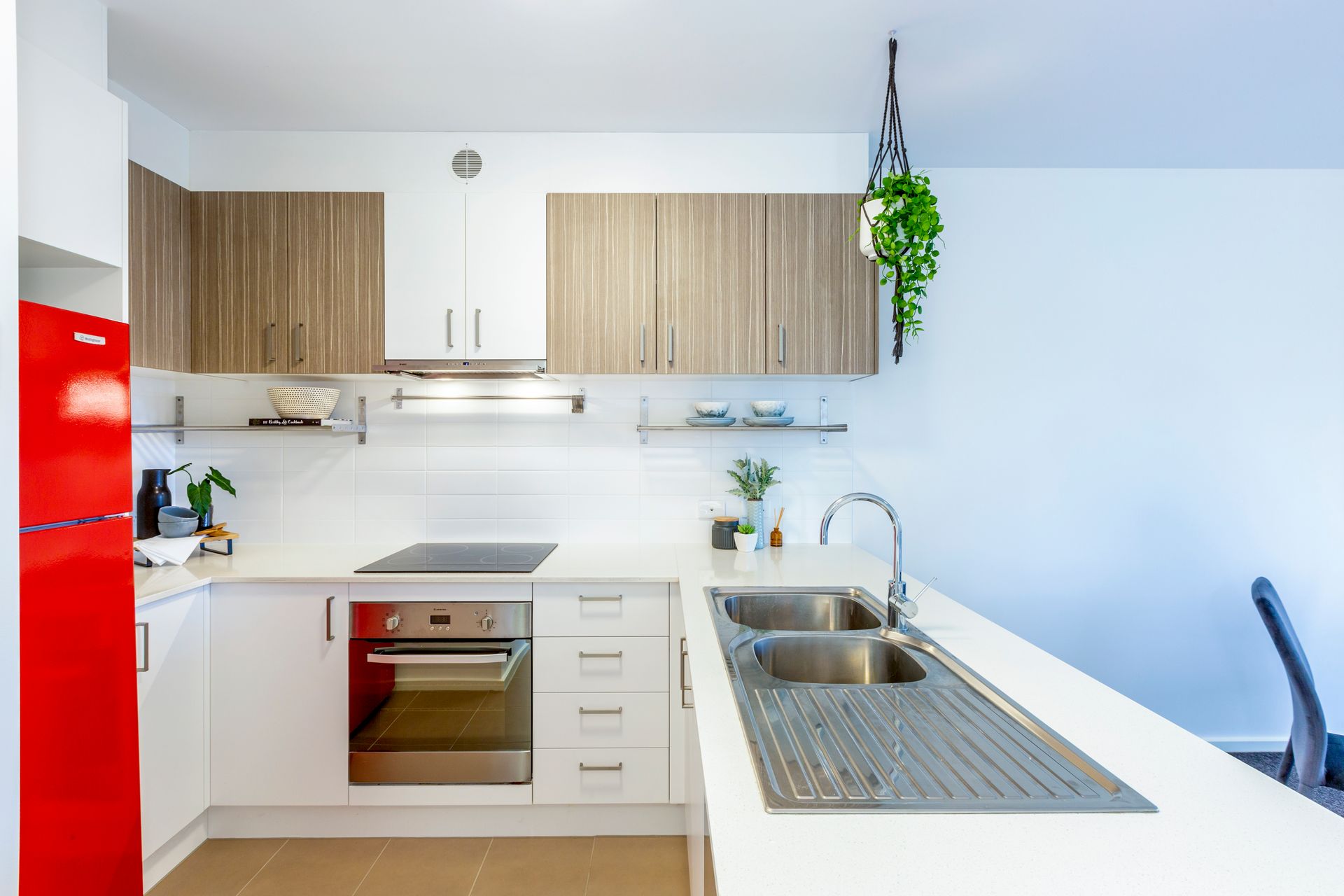 Modern kitchen with white countertops, wooden and white cabinets, stainless steel sink, and red refrigerator.