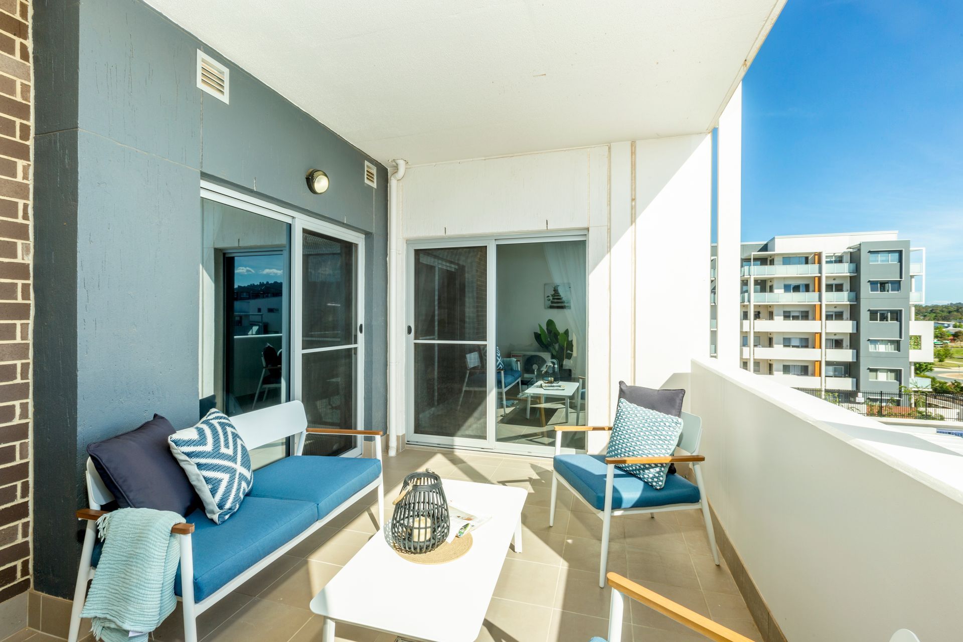 Balcony with blue seating, white table, overlooking buildings on a sunny day.
