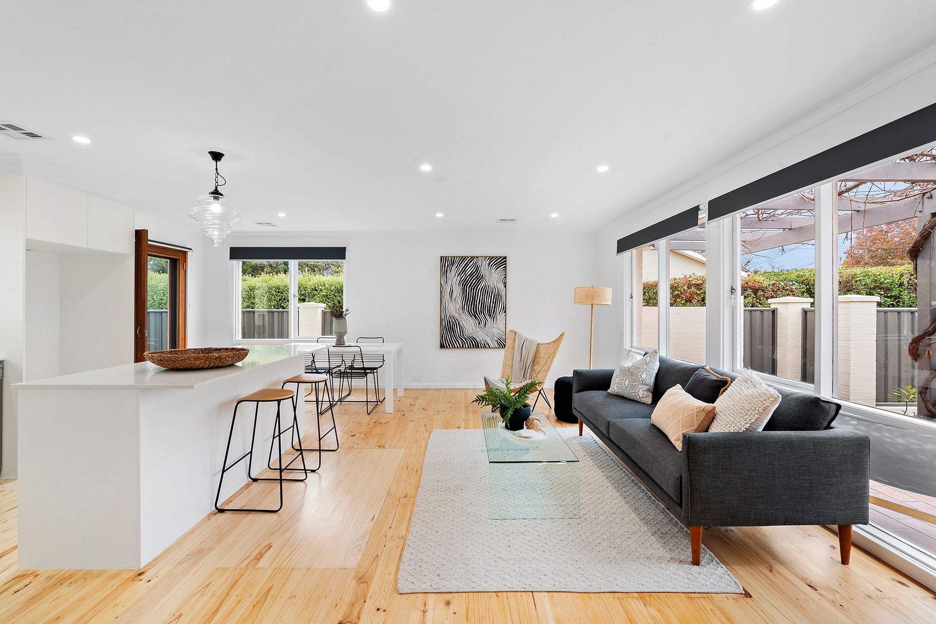 Open-plan kitchen and living area with white cabinetry, island, light wood flooring, and gray sofa.