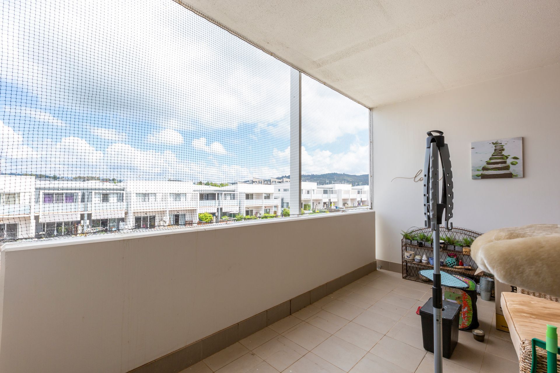 Balcony with safety net overlooking a neighborhood. Interior includes a chair and a storage container.