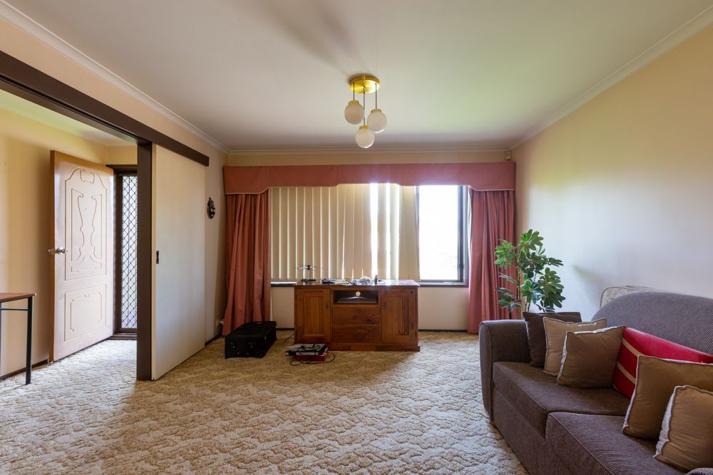 Living room interior with brown sofa, rug, and wooden desk near window with blinds.