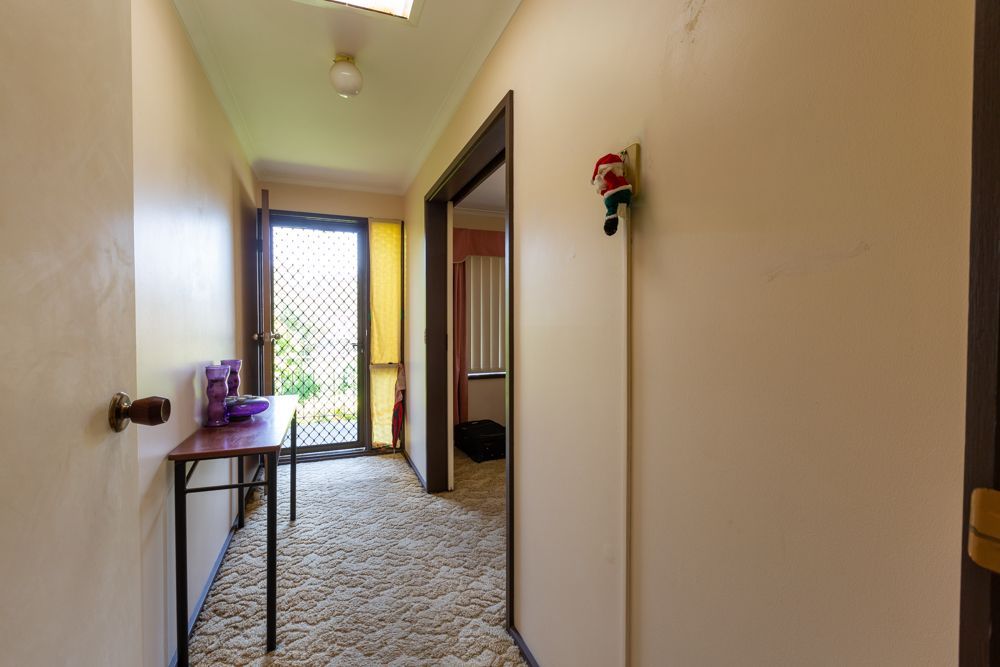 Narrow hallway with beige walls and textured carpet, leading to a door and another room. A table and Santa decoration are visible.