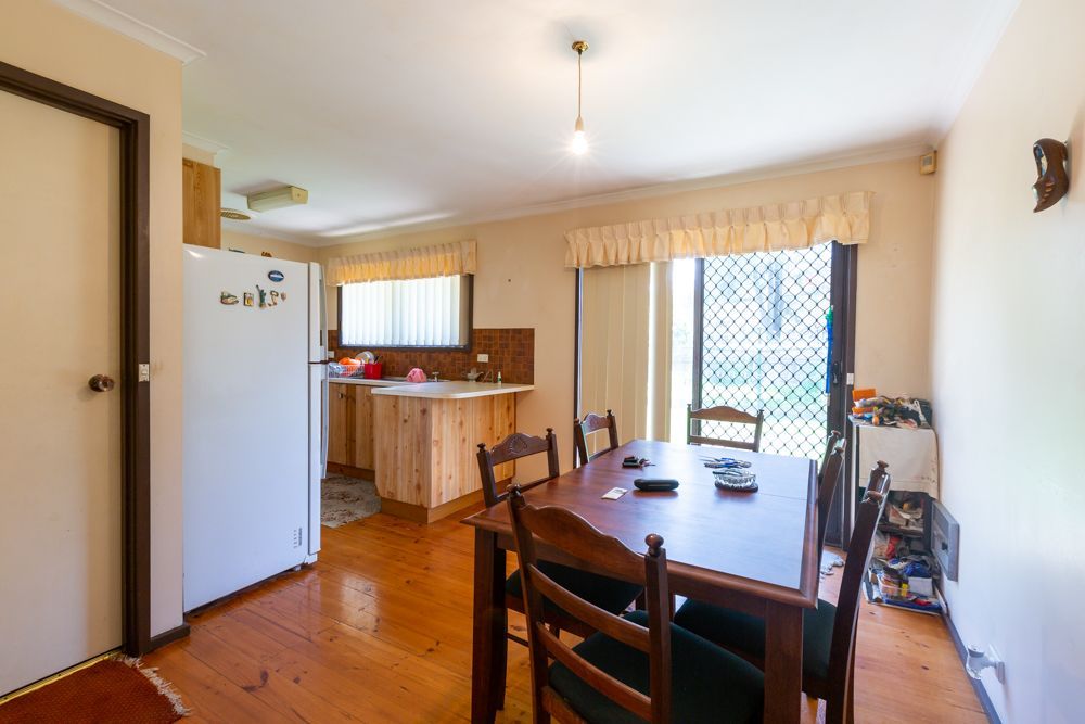 Dining room with a wooden table and chairs, kitchen area visible, sliding door to outside.
