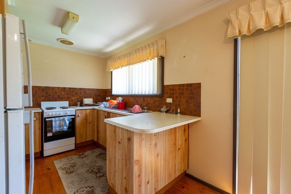 Kitchen with wooden cabinets, beige walls, stove, refrigerator, and a window with blinds.